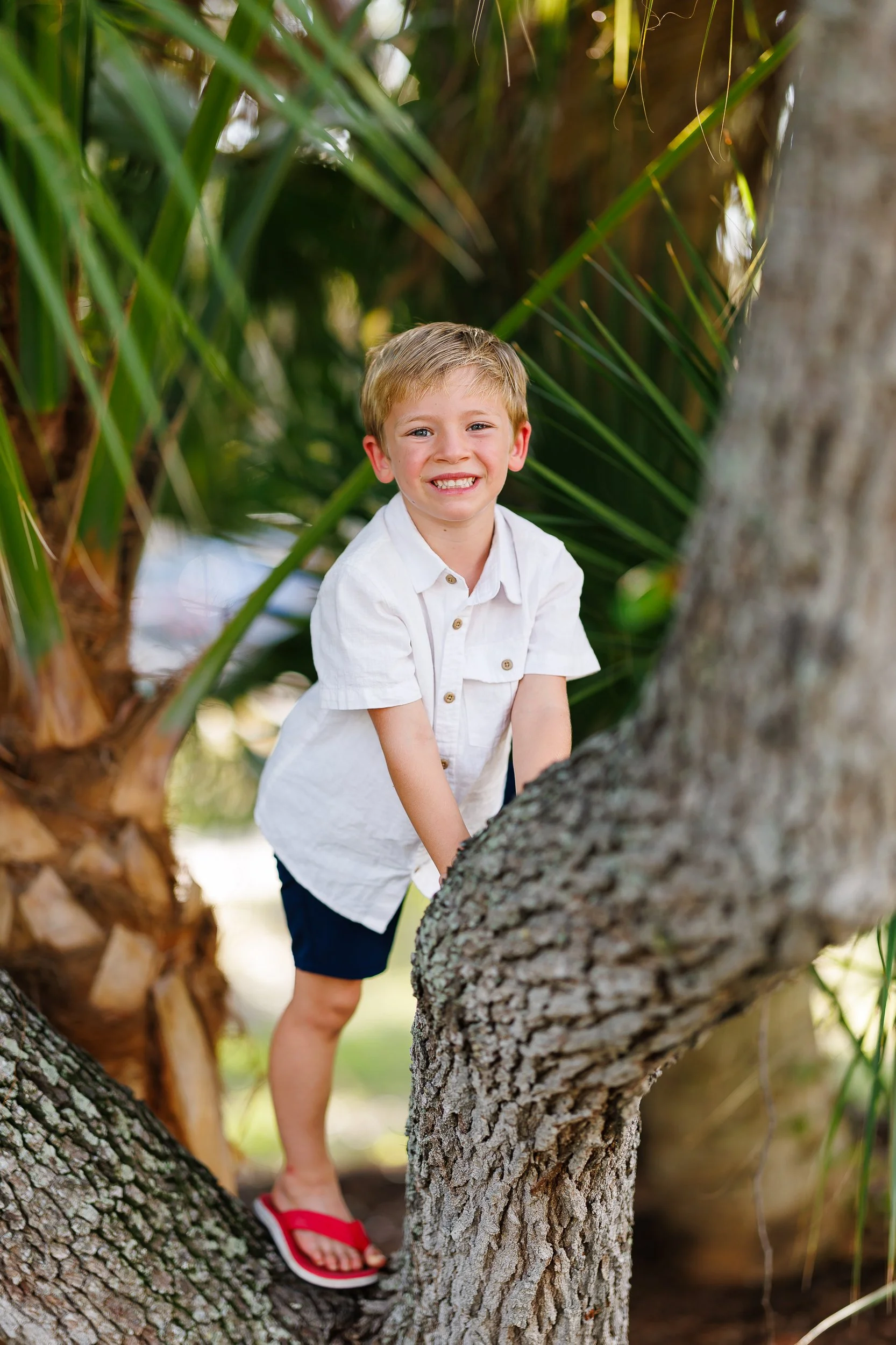 A child in a white shirt smiling against a palm trunk during a Sarasota mini session