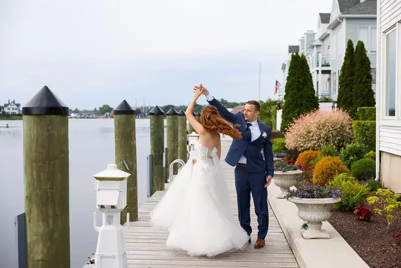 Bride twirling as groom smiles during a candid waterfront wedding portrait on a dock.