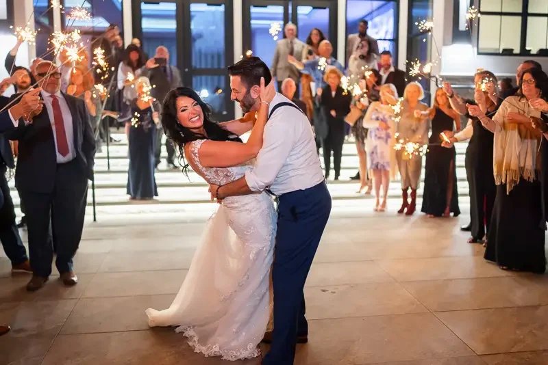 Bride and groom celebrate their wedding exit surrounded by guests holding sparklers outside a waterfront venue