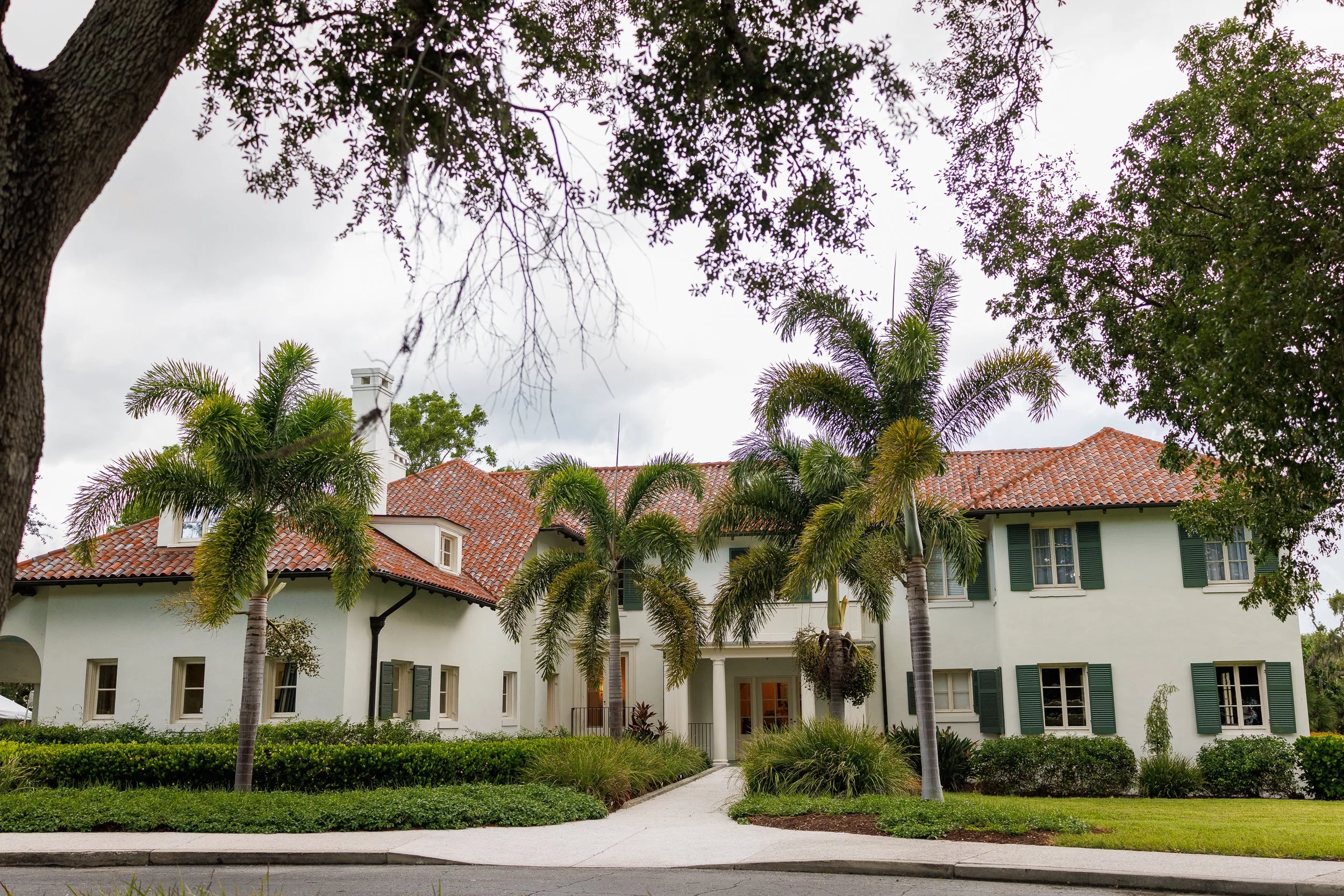The Edson Keith Mansion at Phillippi Estate Park, a cream stucco house with a red barrel-tile roof and green shutters, behind royal palms.