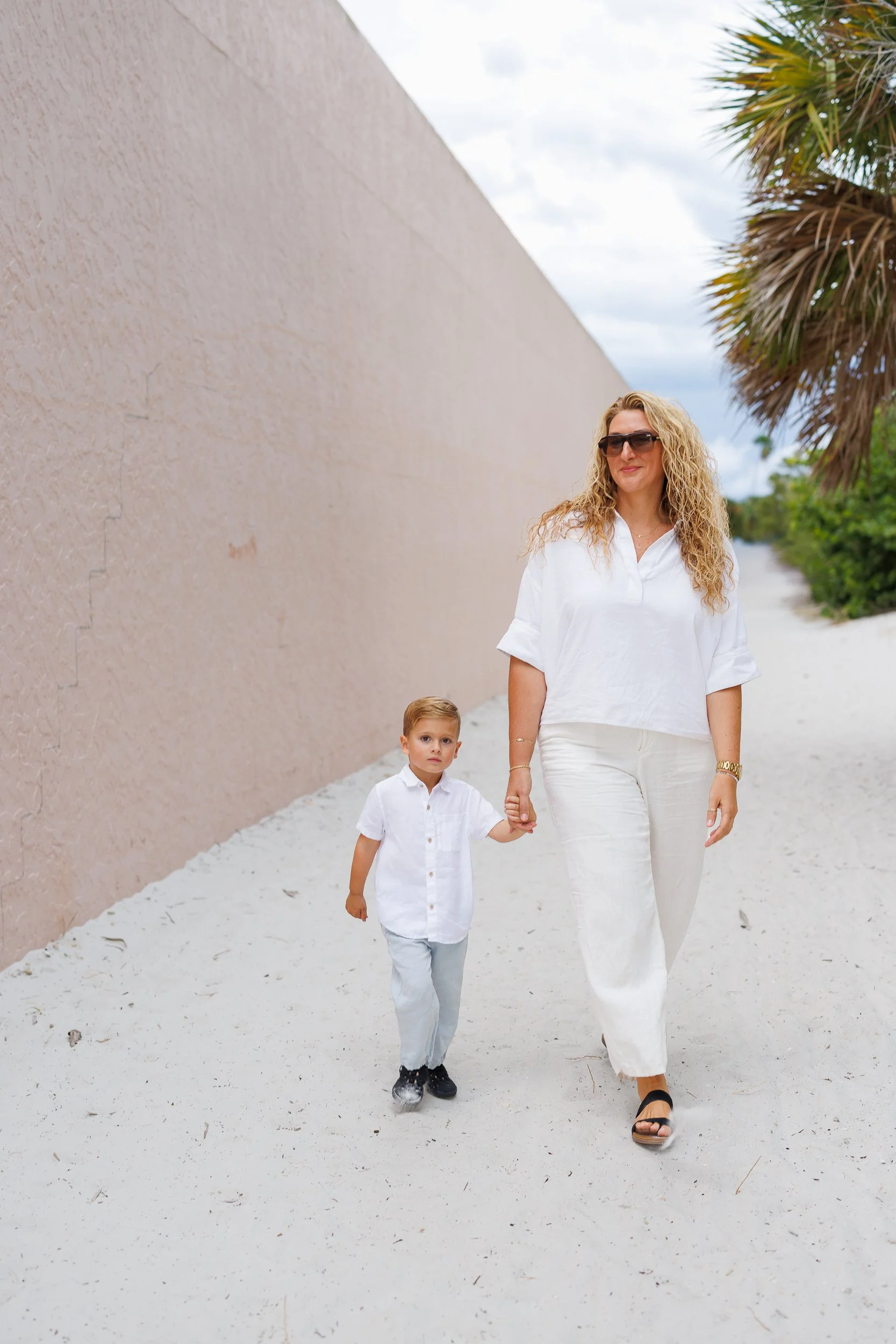 A person and a child walking hand in hand on a sandy path.