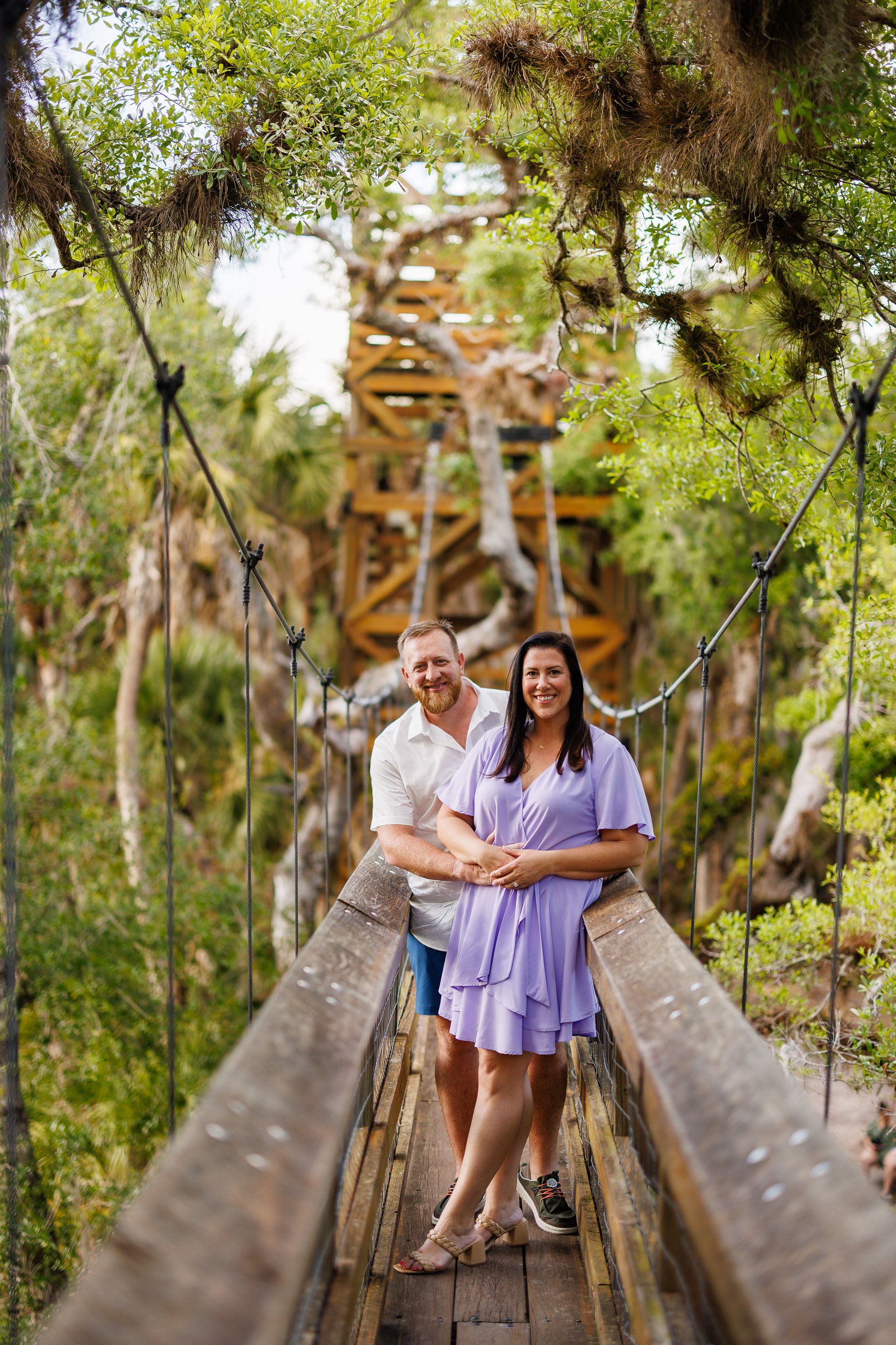 Will and Erin standing together on the suspension bridge at Myakka River State Park, the wooden observation tower behind them.