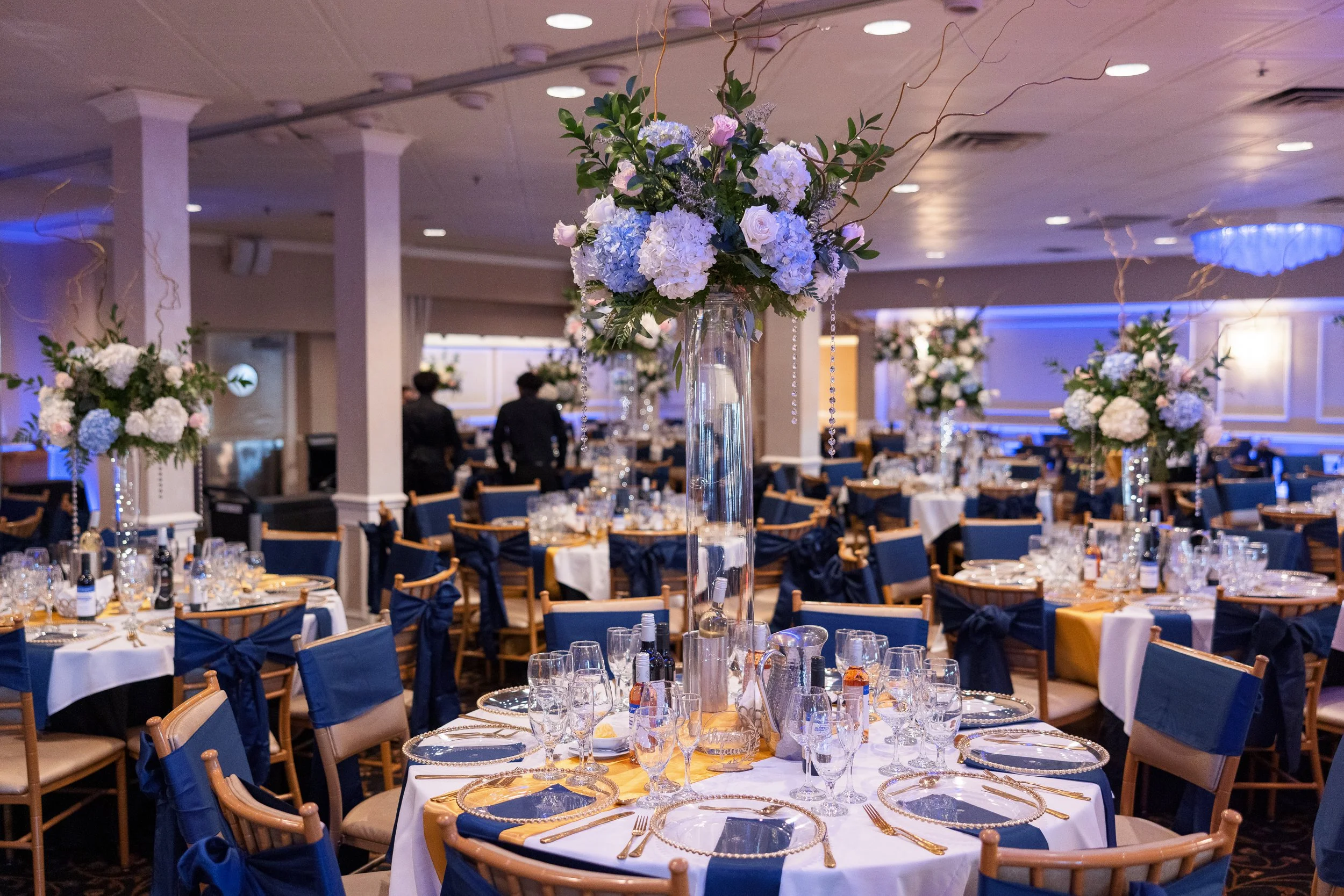 Round banquet tables set with tall blue and white floral centerpieces at a corporate gala.