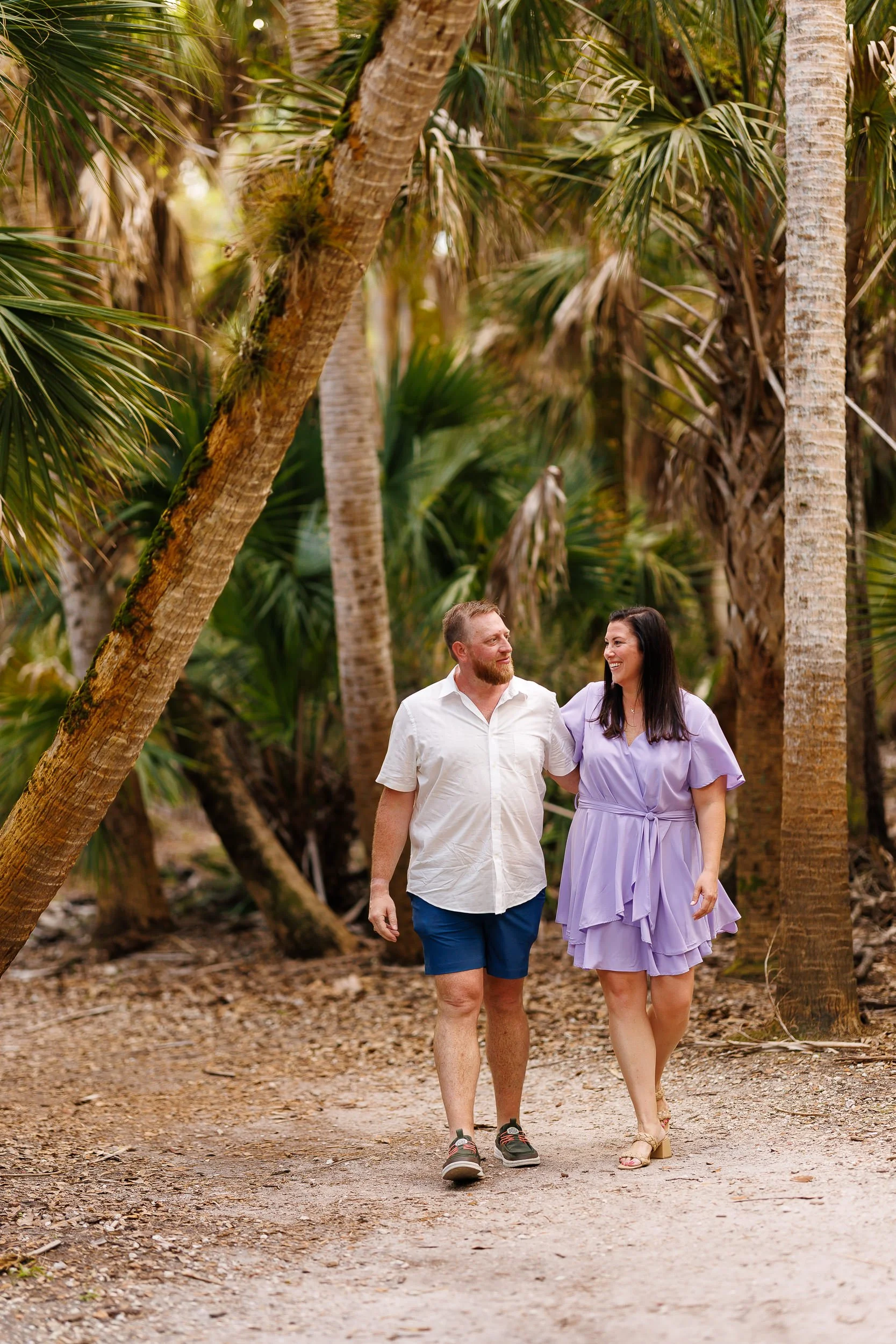 Will and Erin walking arm in arm down a sandy trail under tall sabal palms at Myakka River State Park.