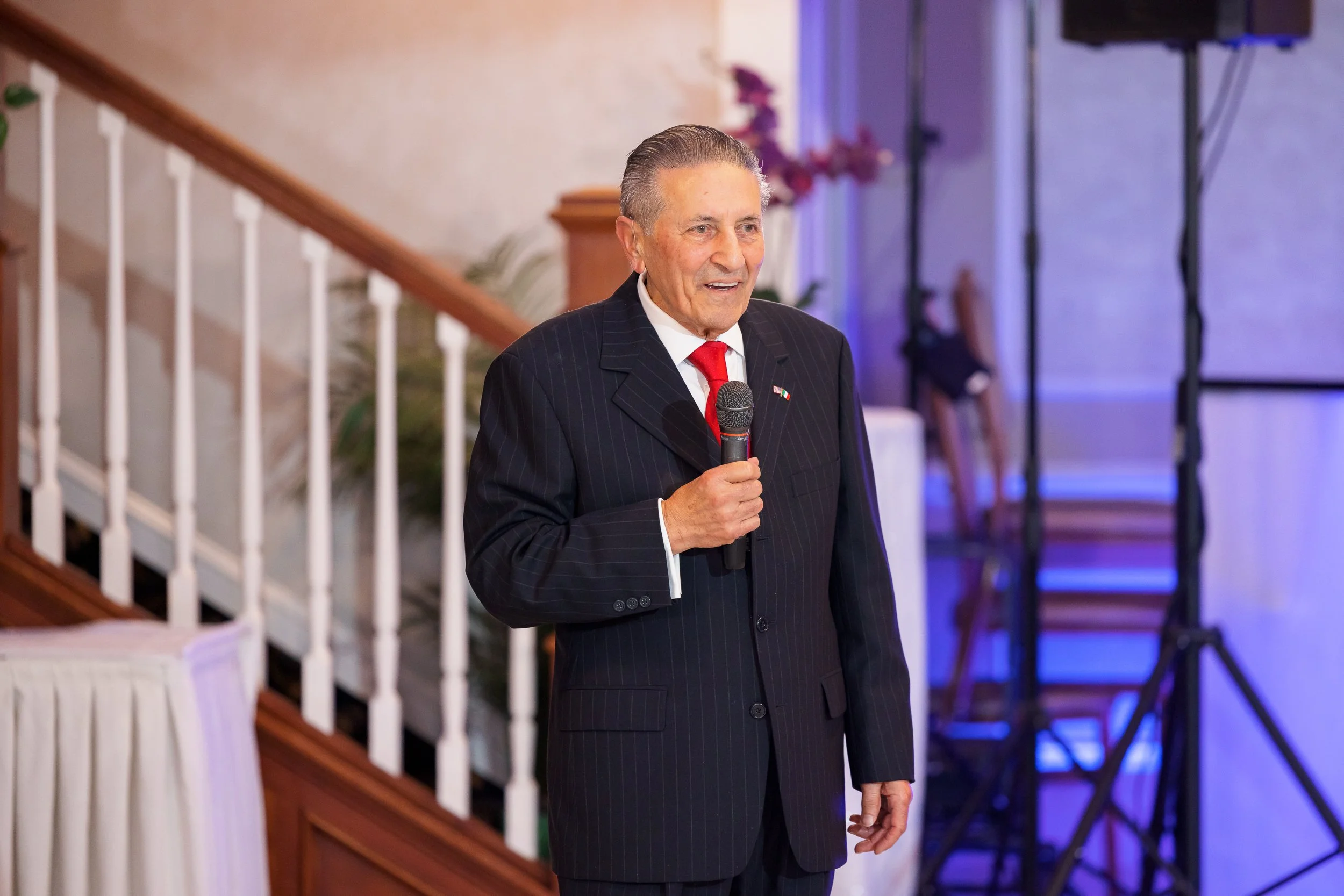A speaker in a dark suit holding a microphone at a company anniversary gala.