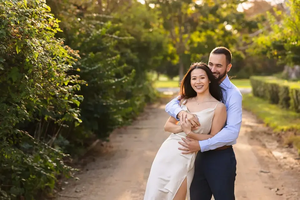 A natural engagement portrait of a couple holding each other on a quiet forest trail, filled with soft light and relaxed emotion.