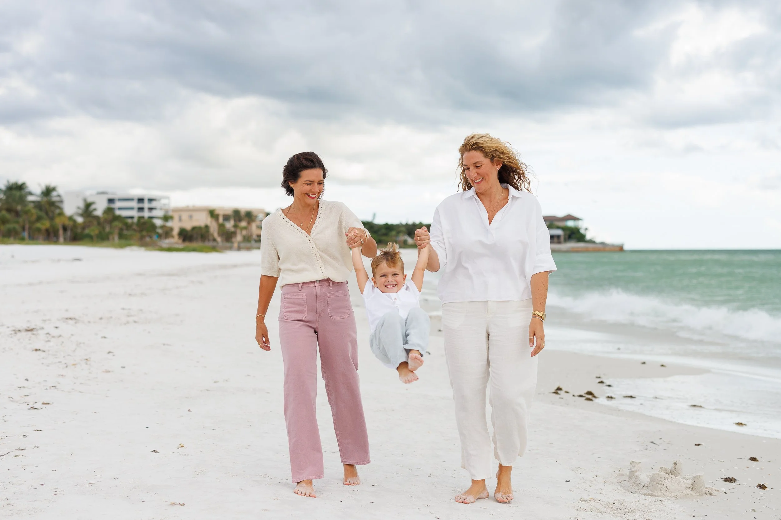 Two people walking on a beach holding hands with a child between them.