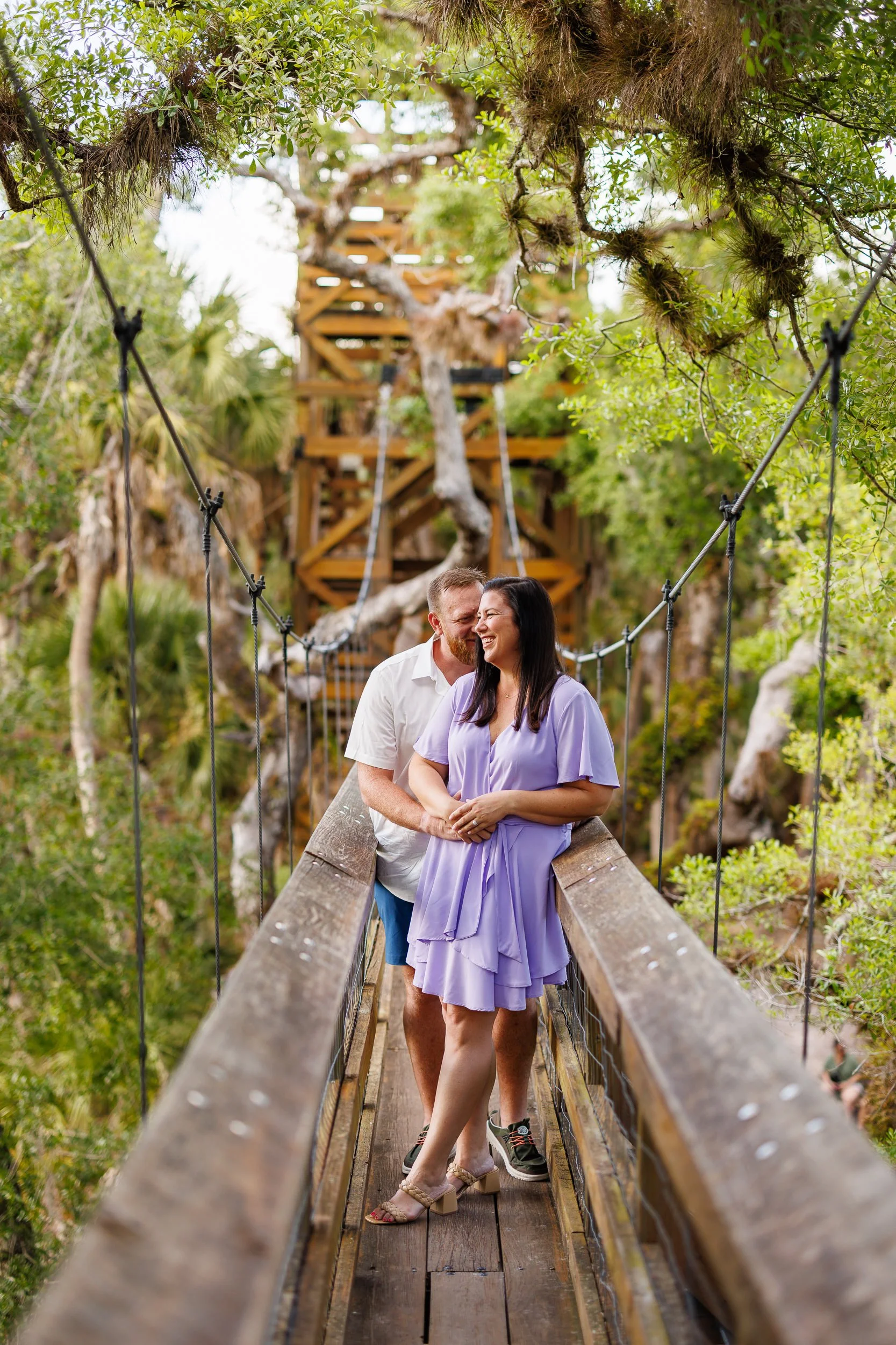 Will leaning in to Erin's cheek on the Myakka canopy walkway bridge, both laughing, oak branches overhead.