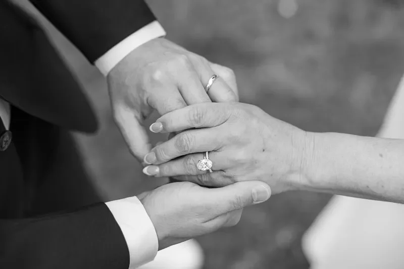 A black-and-white photo of two people holding hands, both wearing rings, with one hand gently holding the other's.