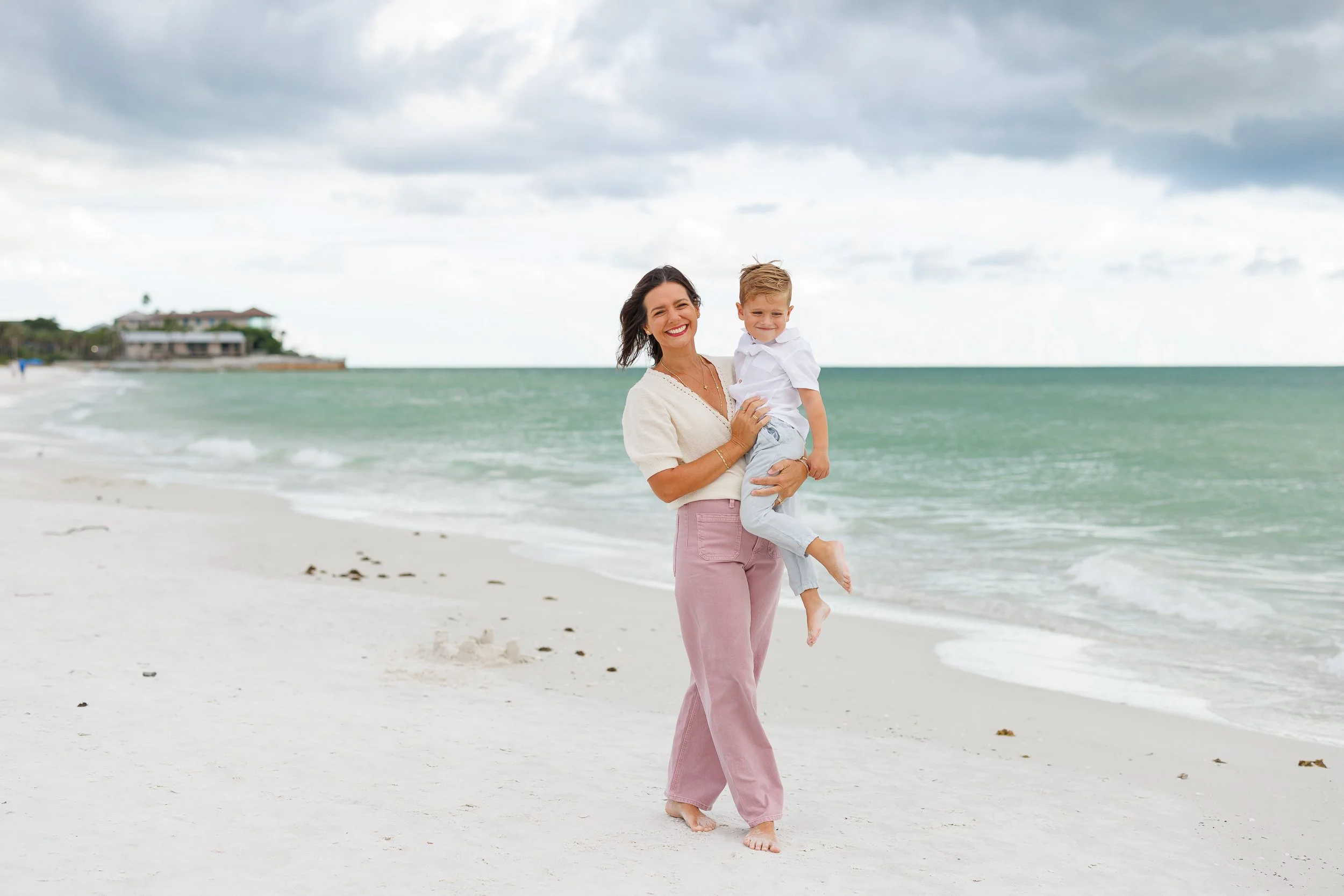 A parent holding a child at the water's edge during a Sarasota beach mini session