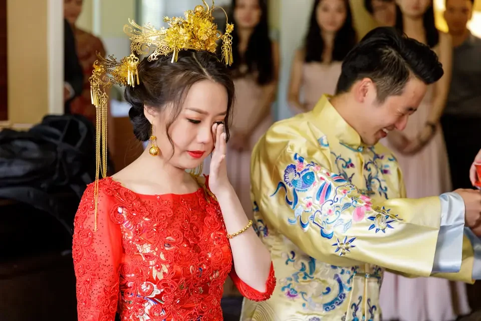 Bride becomes emotional during a traditional Chinese wedding tea ceremony while wearing a red embroidered dress and gold hairpiece.