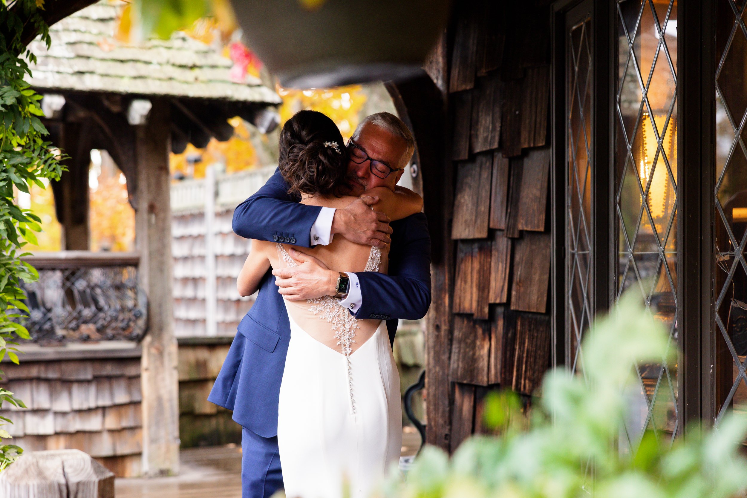 A bride and her father holding each other in a long hug on a covered porch after their first look.