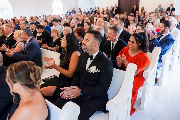 Wedding guests inside a ceremony space reacting with smiles and emotion, creating an atmosphere of connection and shared experience.