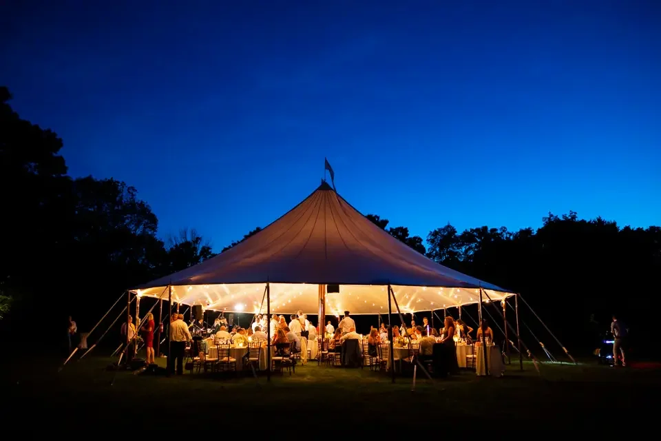 Nighttime view of a glowing tented wedding reception at Smith Farm Gardens with guests dining under string lights.