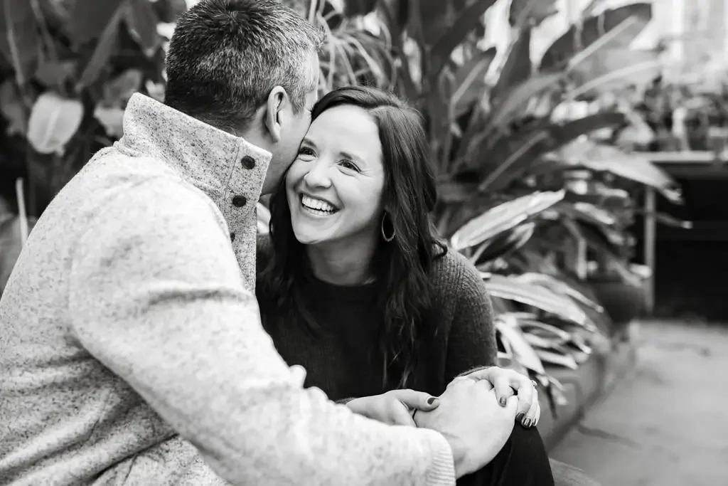 Couple laughing together during a candid engagement session, sharing a relaxed and genuine moment without posing