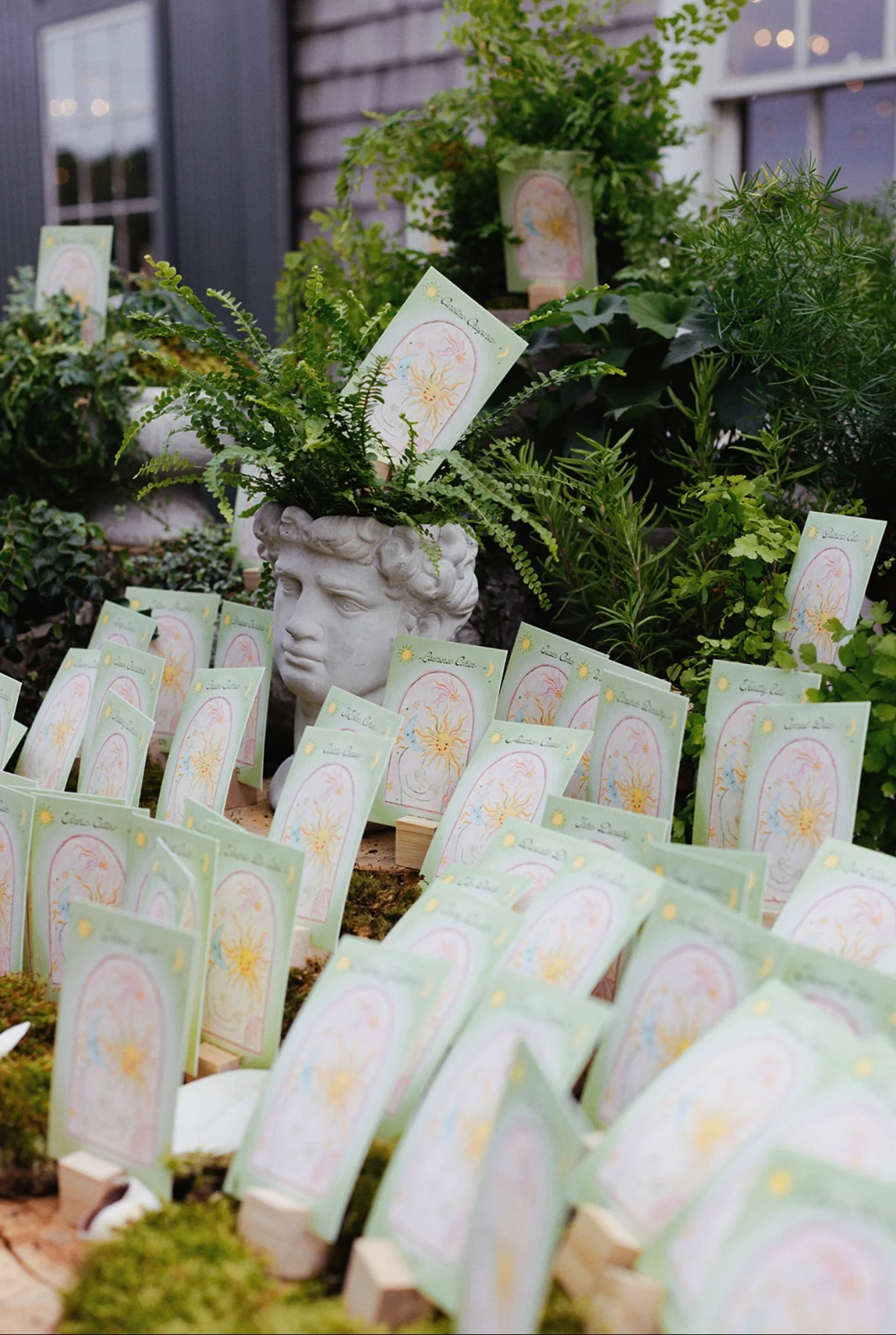 Decorative plant arrangement withescort cards featuring a sun and moon design, placed in a garden setting near a house.