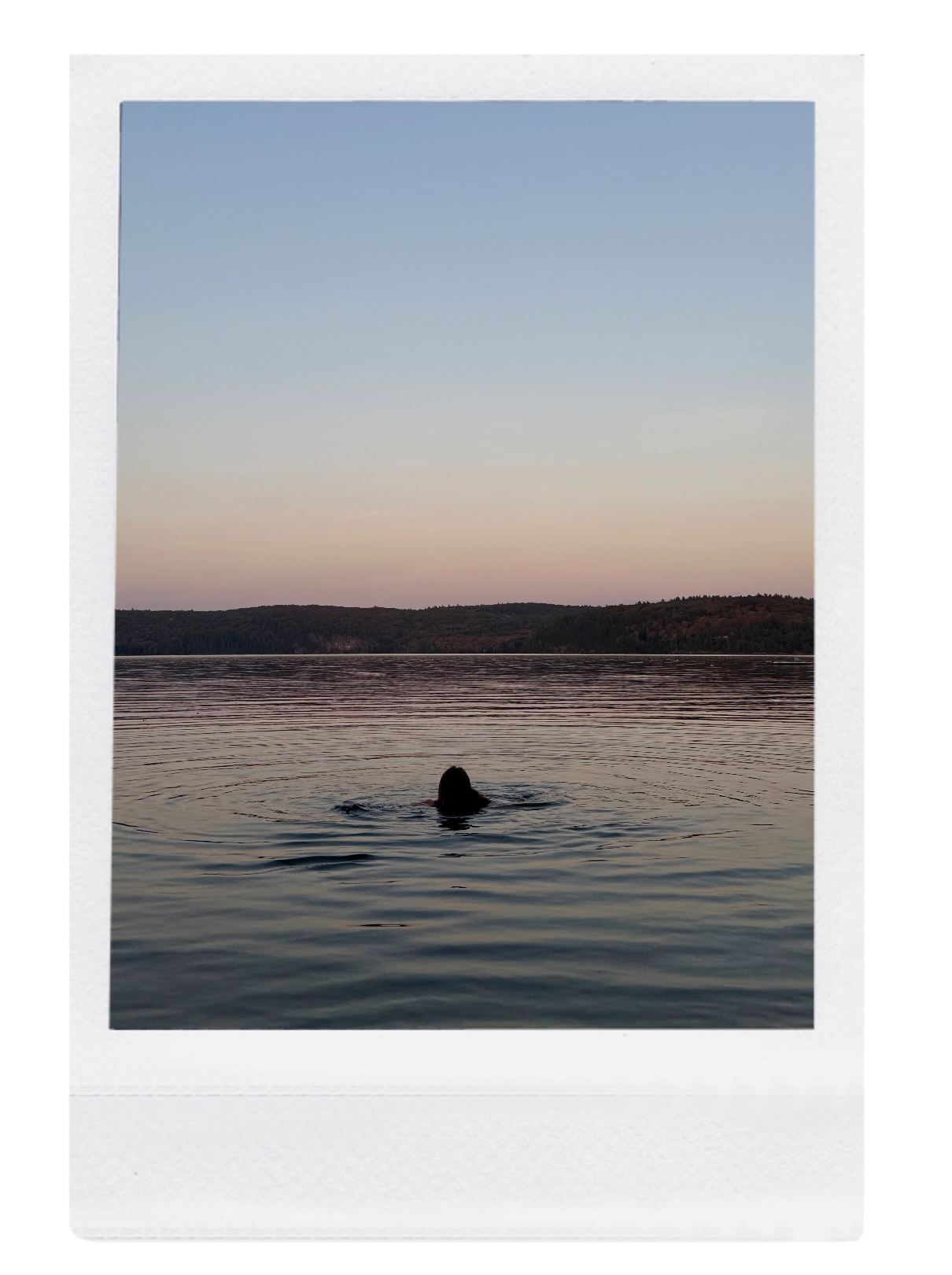 A person swimming in a lake during sunset with a background of hills and a clear sky.
