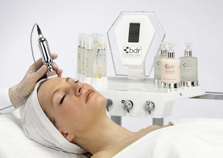 A woman lying down while receiving facial treatment with a handheld device near her forehead.