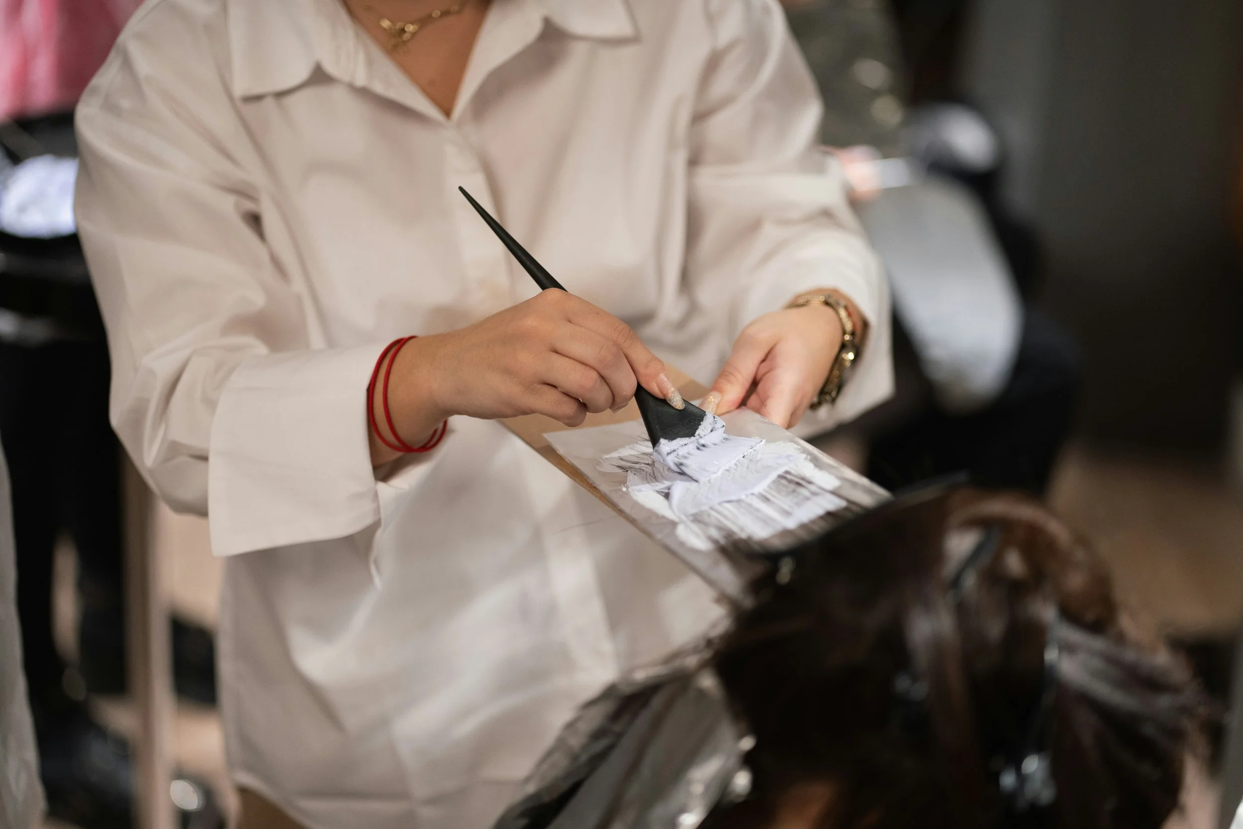 A person applying hair dye on a client using a brush.