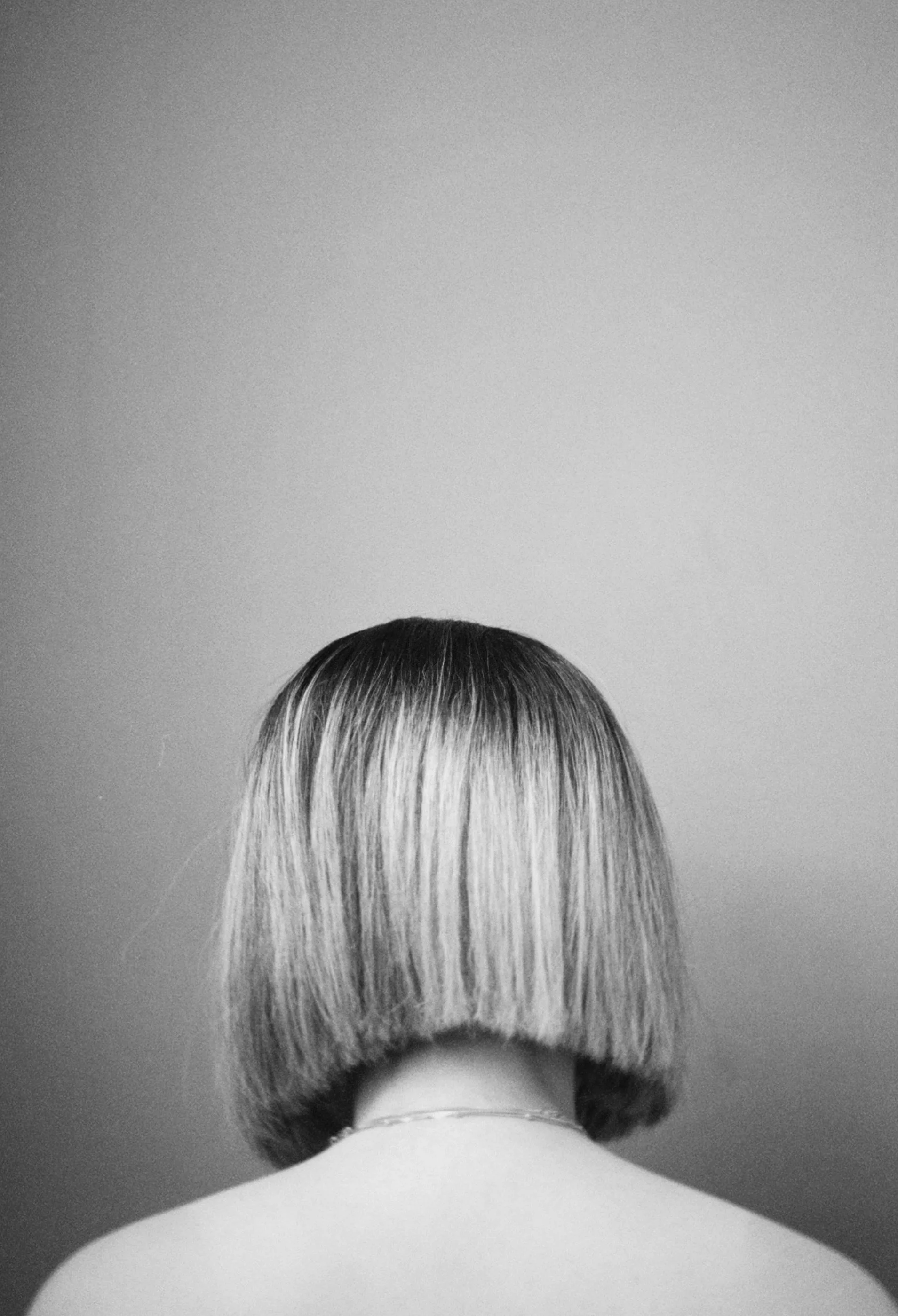 Back view of a woman with a bob haircut, facing a plain wall