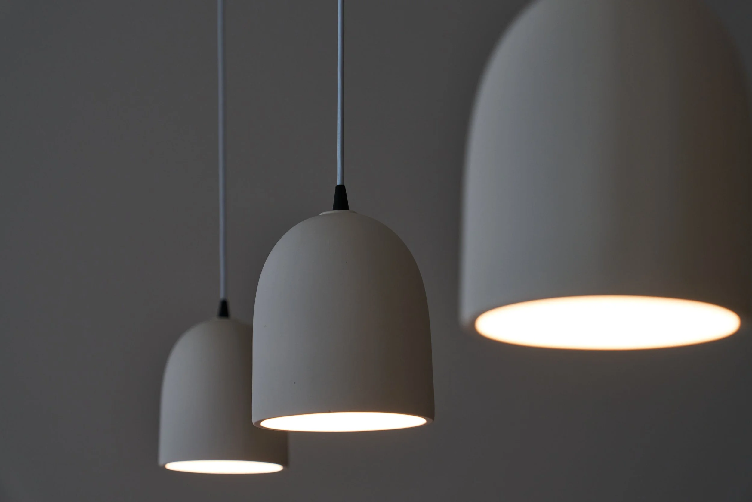 Three modern white pendant lights hanging from the ceiling, one of which is turned on, casting a soft glow.
