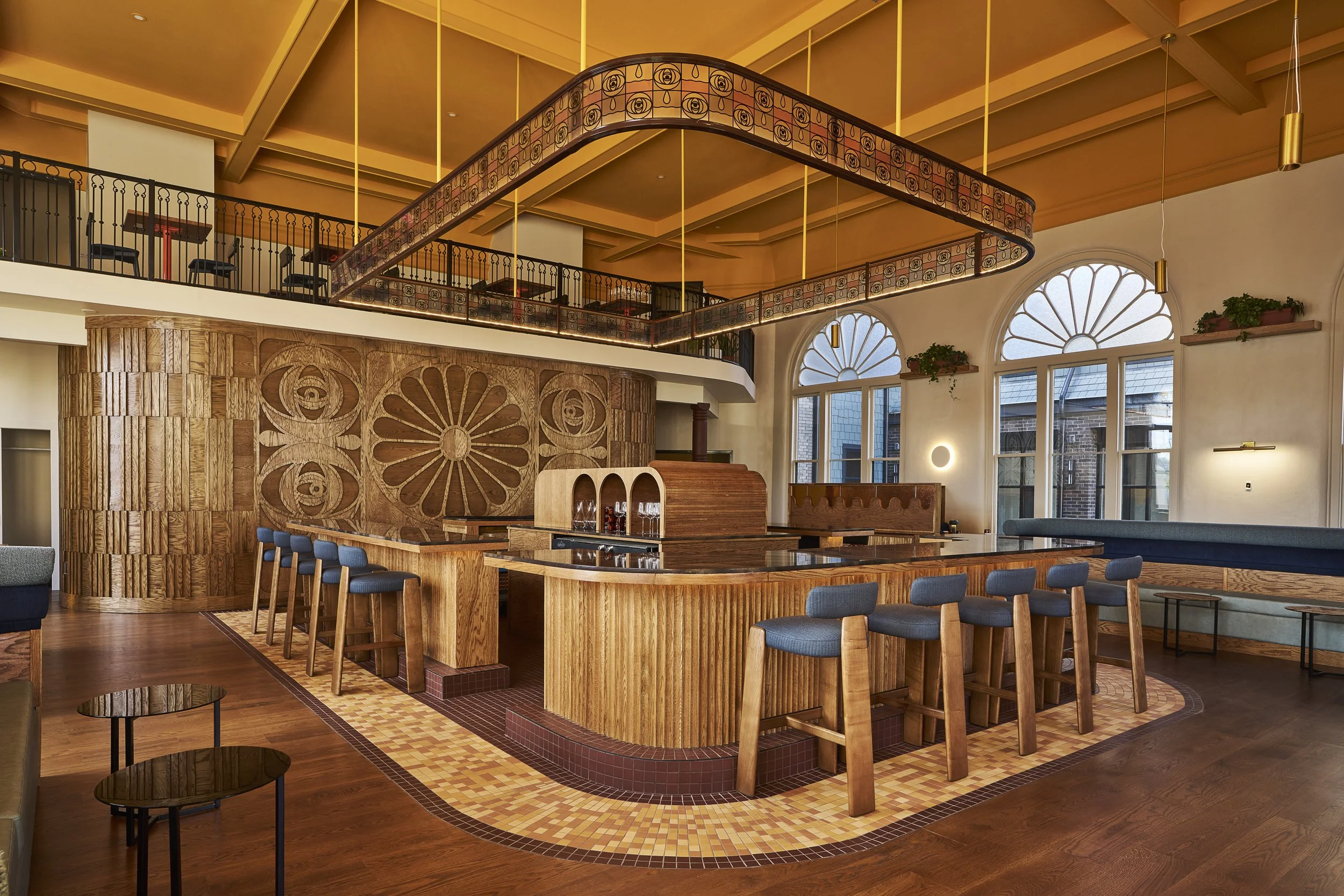 Interior of a stylish restaurant or cafe with wooden furniture, a bar counter, large arched windows, and modern lighting fixtures.