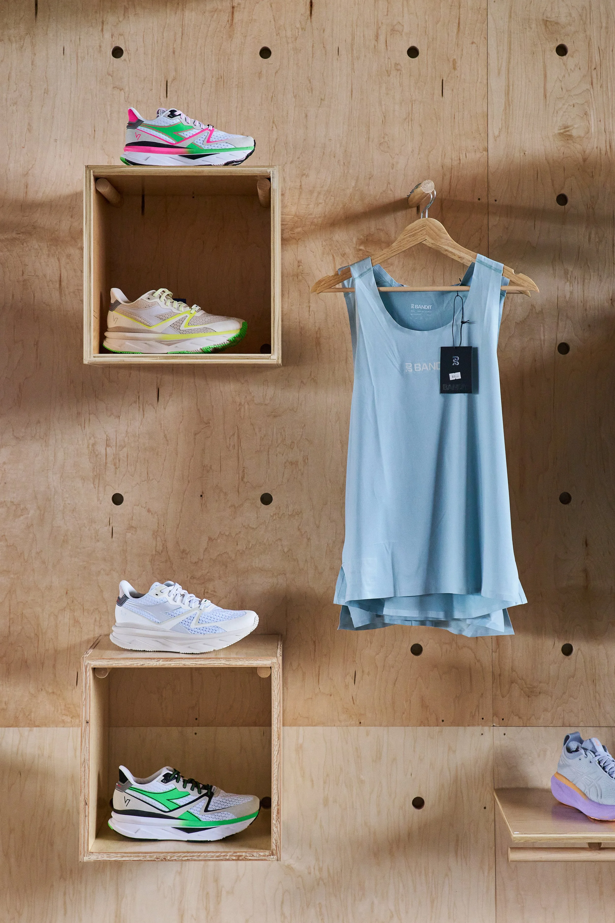 Display of athletic shoes, sleeveless top on hanger, against a wooden wall with cubby shelves.