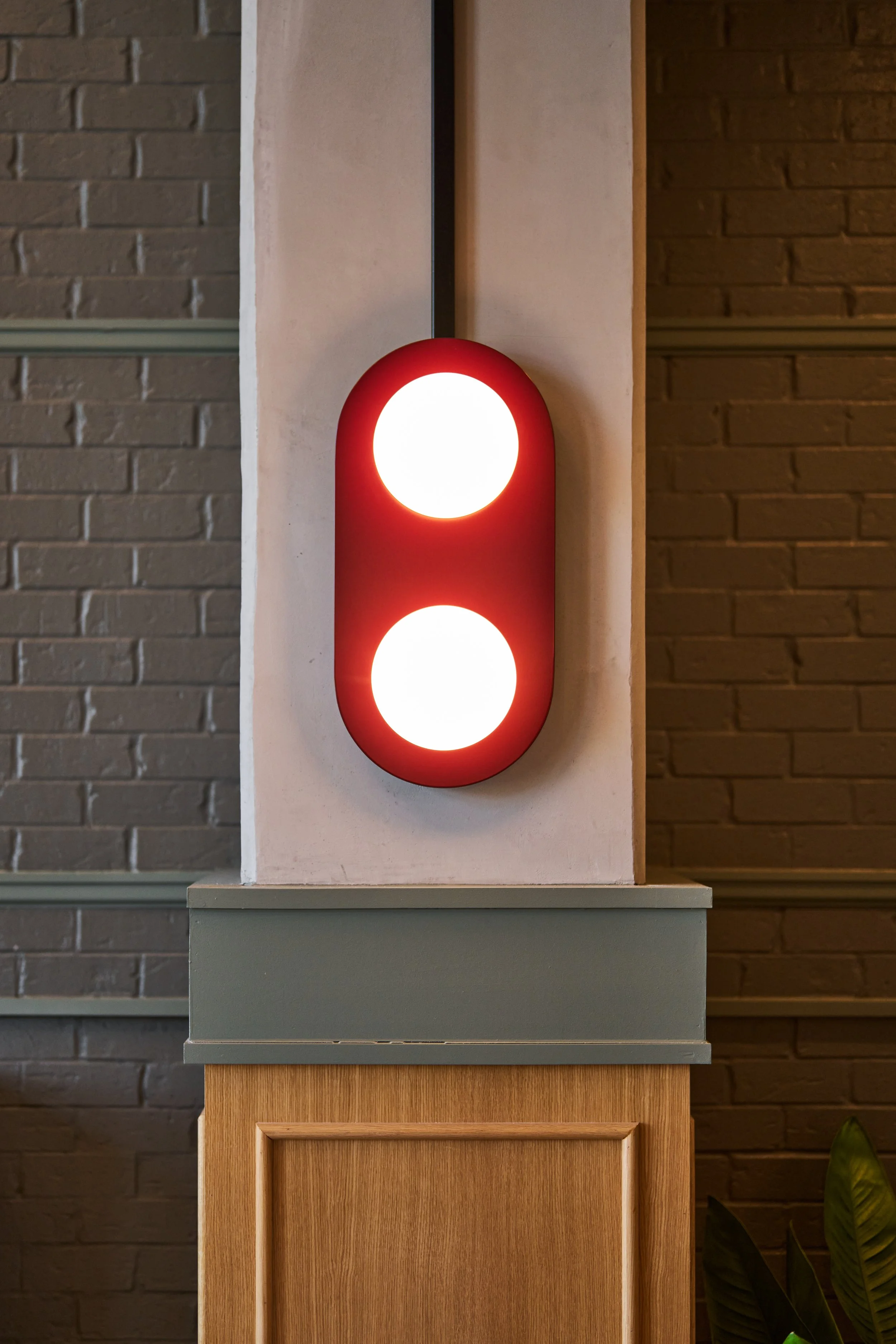 A vertical traffic light with two illuminated white lights, mounted on a white rectangular wall, with a brick wall background.
