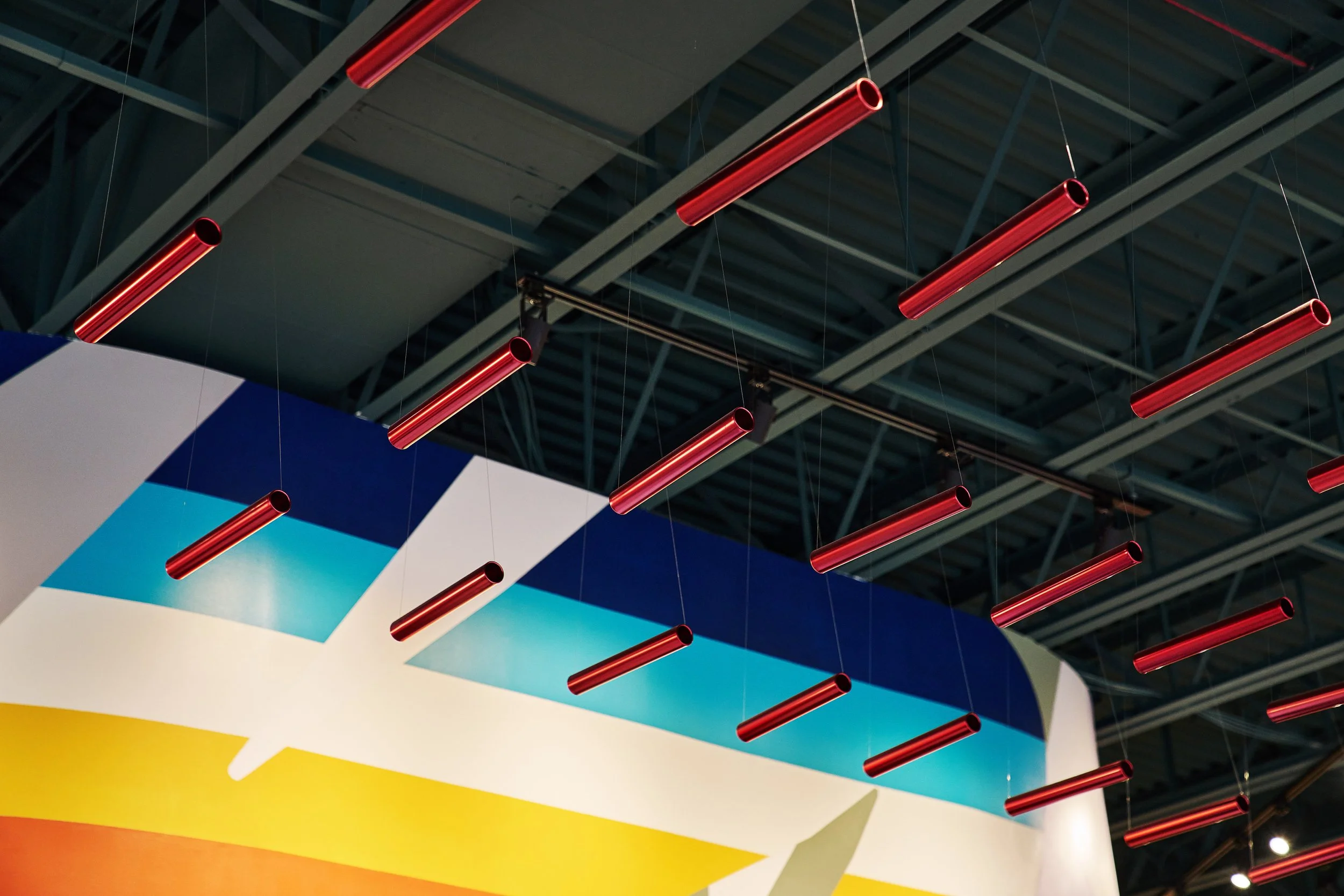 Ceiling with multiple red cylindrical hanging lights and colorful geometric wall design.