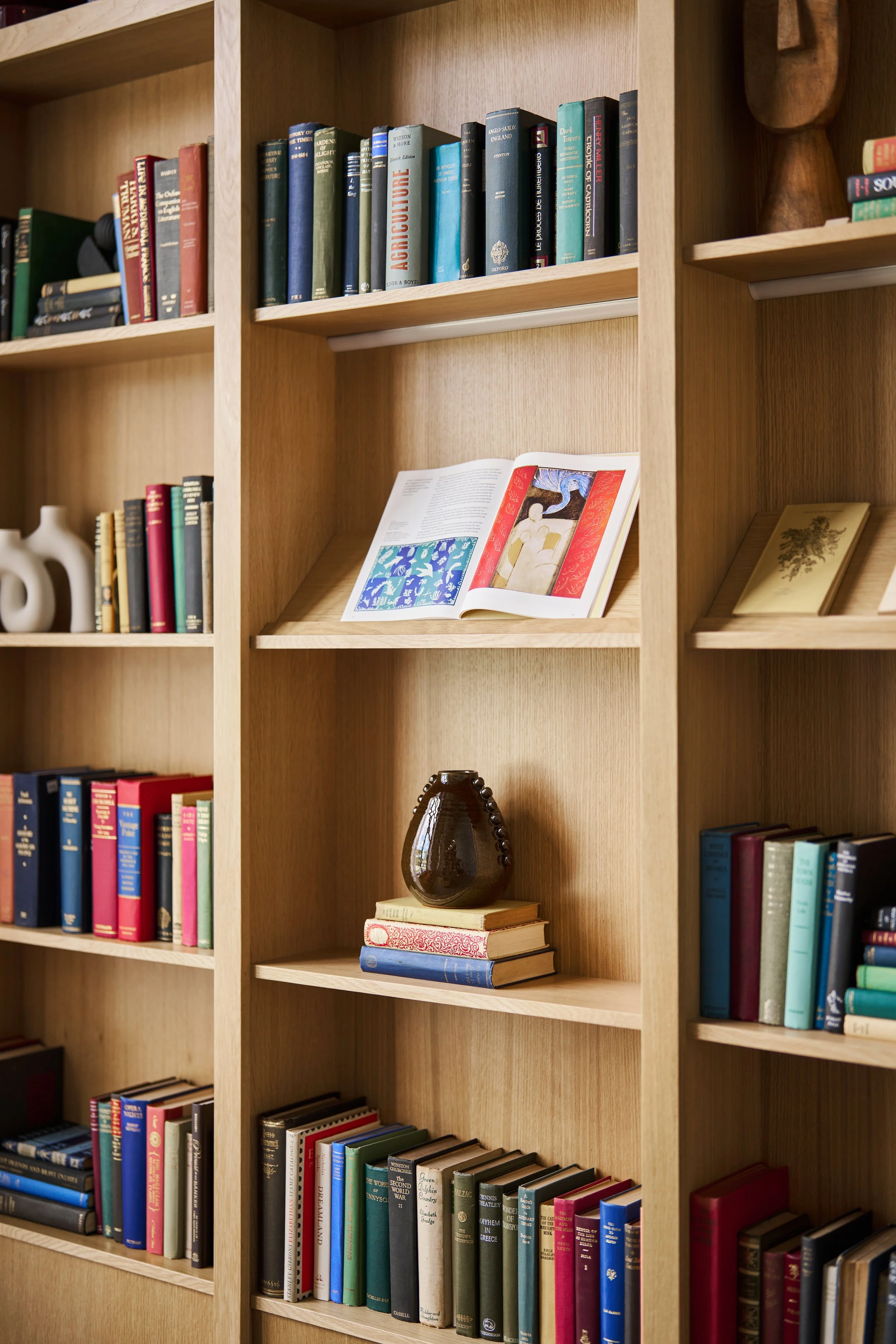 A wooden bookshelf with various books, an open art book, a decorative vase, and a photo frame.