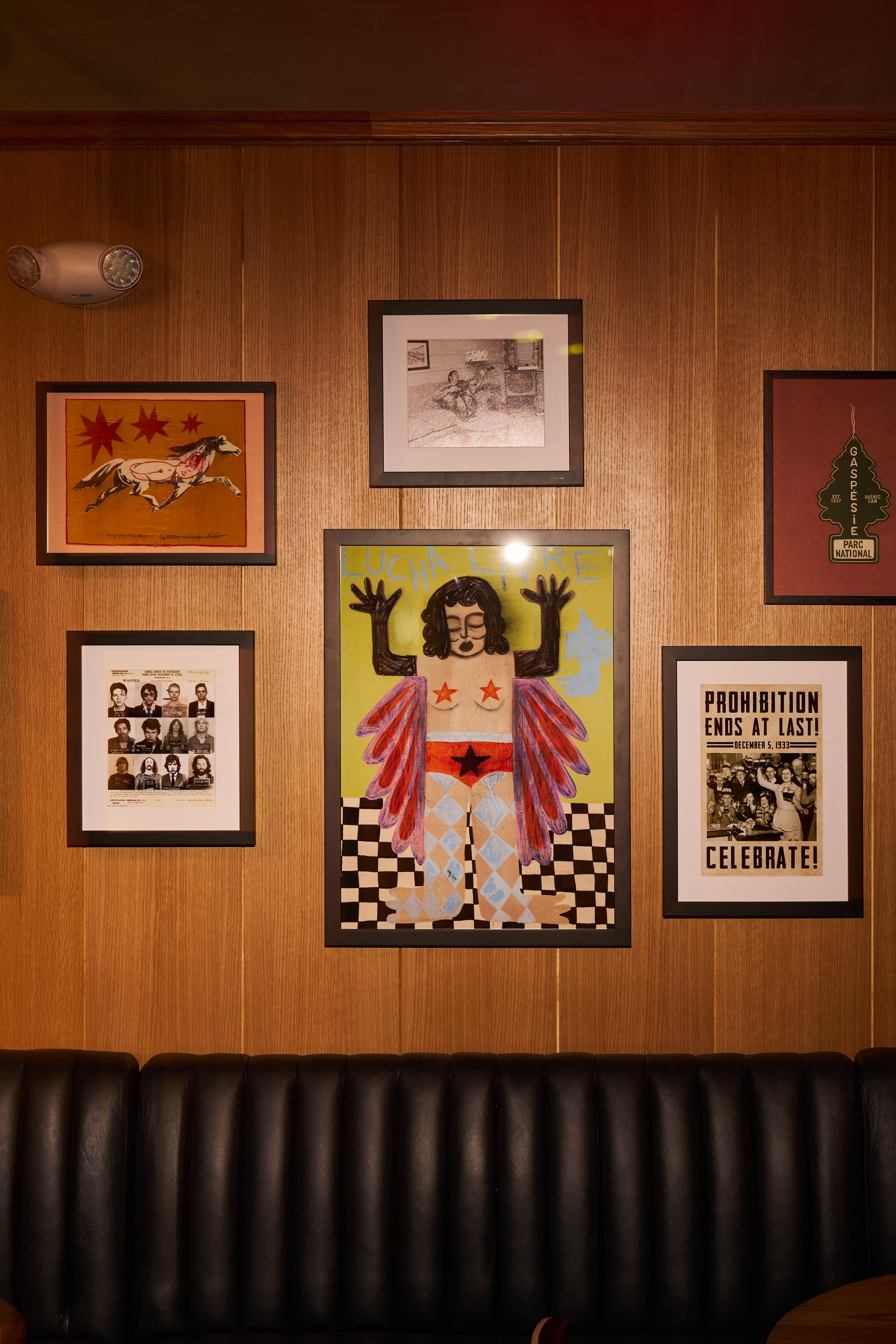 A wooden wall decorated with various framed art posters, including a portrait of a woman with arms raised, a black and white vintage photo, a poster with a horse illustration, and a protest or celebration poster with the text "Prohibition Ends at Las