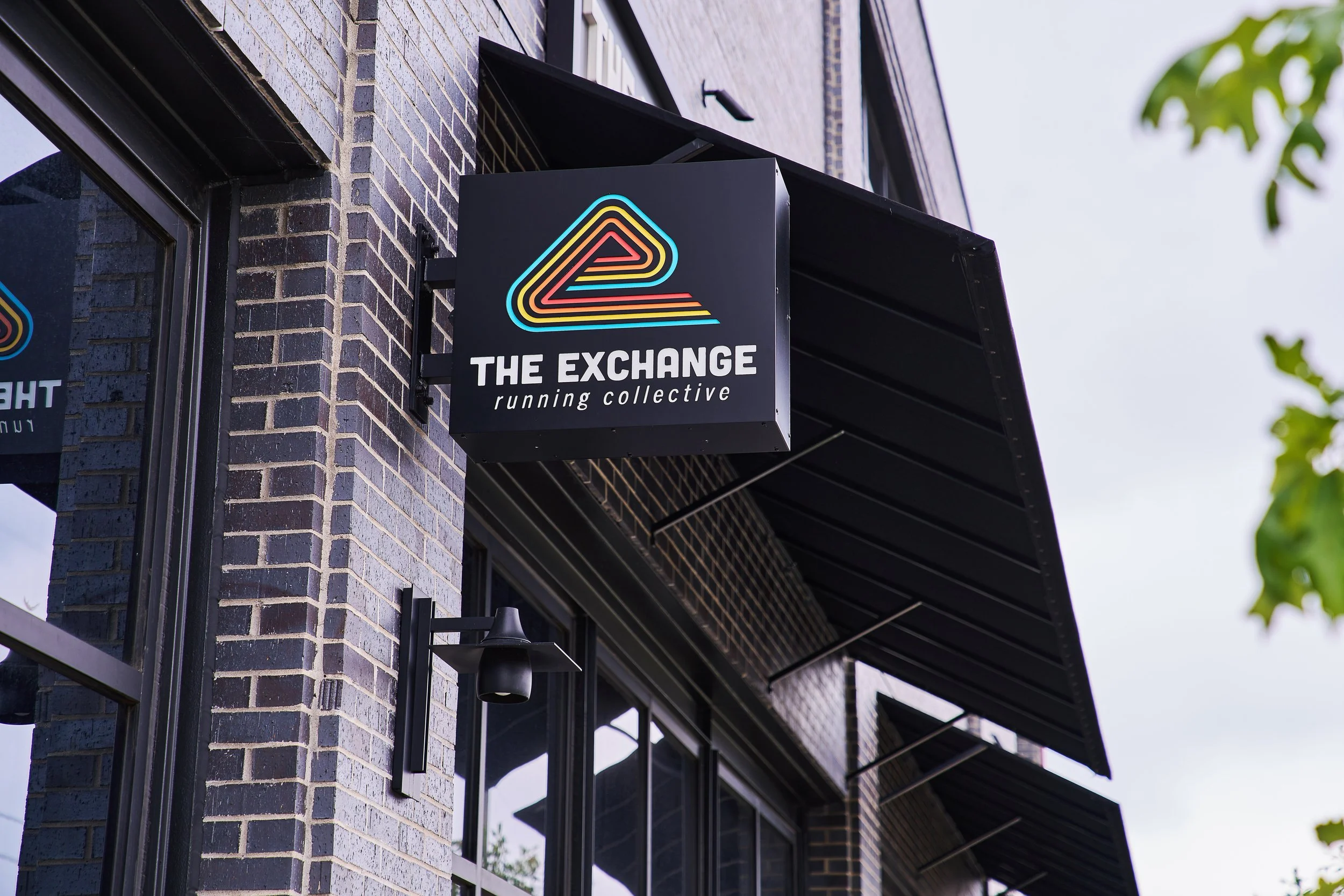Signboard attached to the brick building reads "THE EXCHANGE running collective" with a colorful neon triangle logo above it.