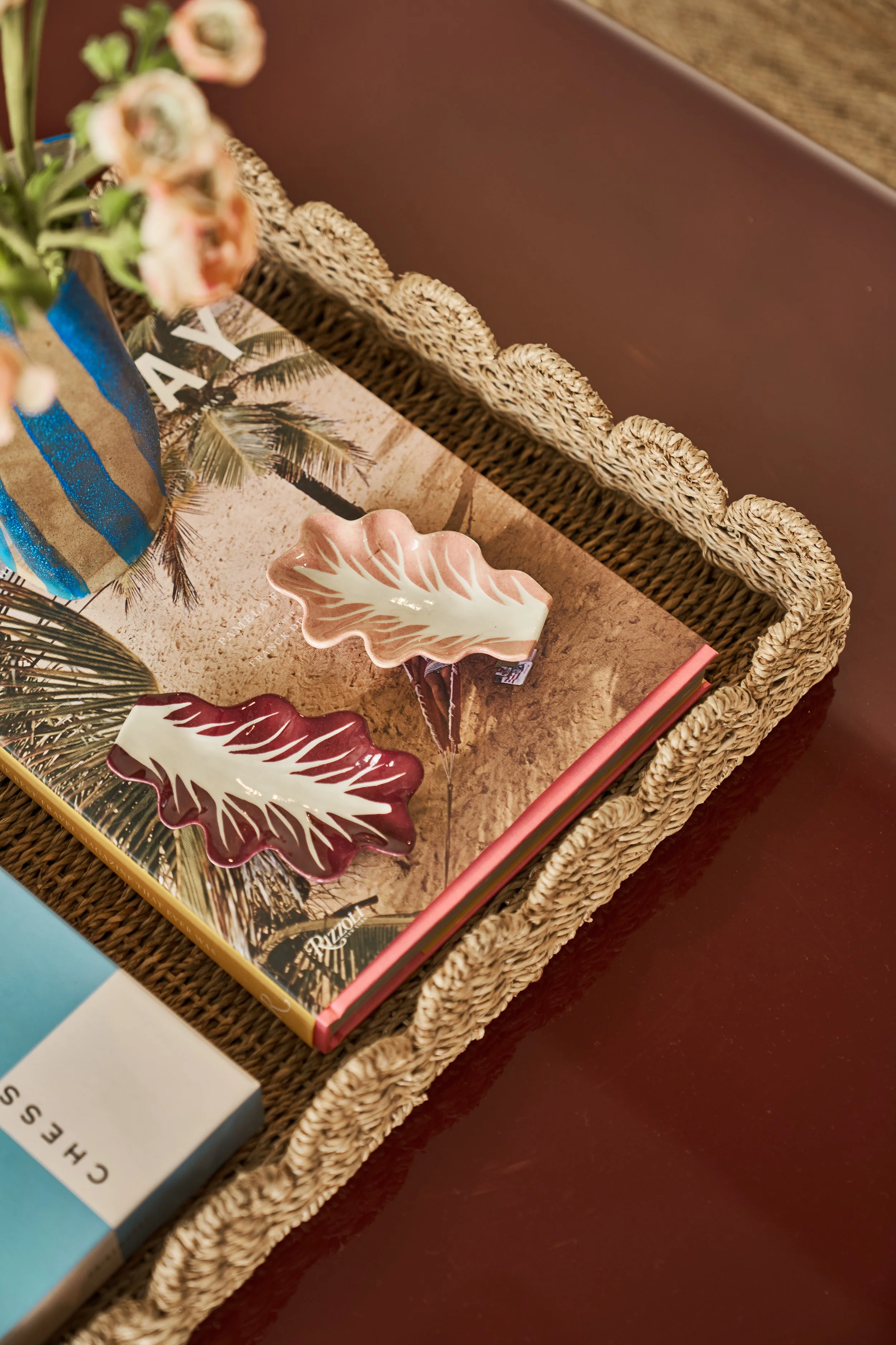 Decorative cracked leaf-shaped plates on a tray with a tropical-themed magazine or book underneath, and a vase with flowers partially visible in the background.