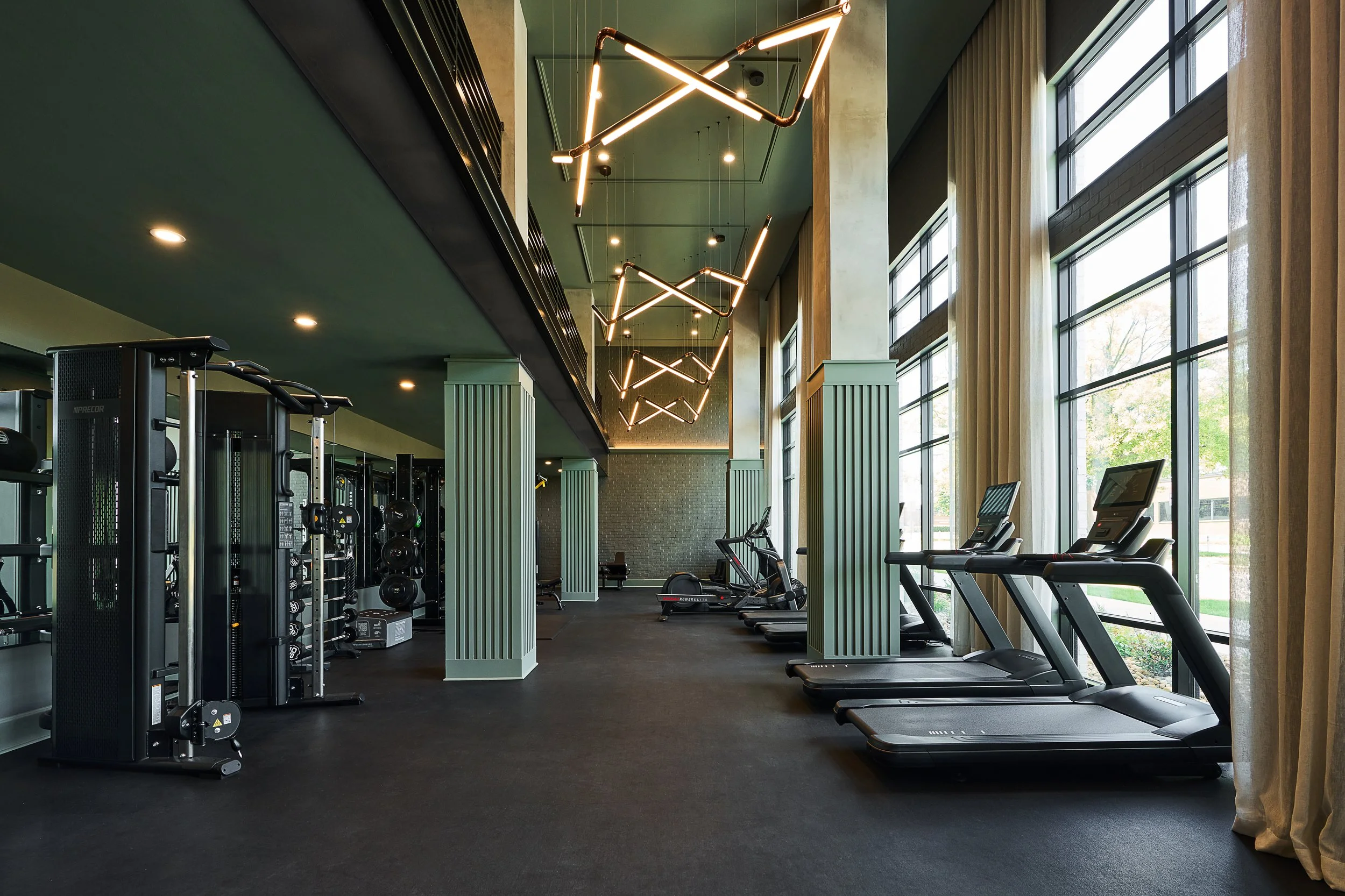 Modern gym interior with large windows, treadmill machines, free weights, and stylish ceiling lights.