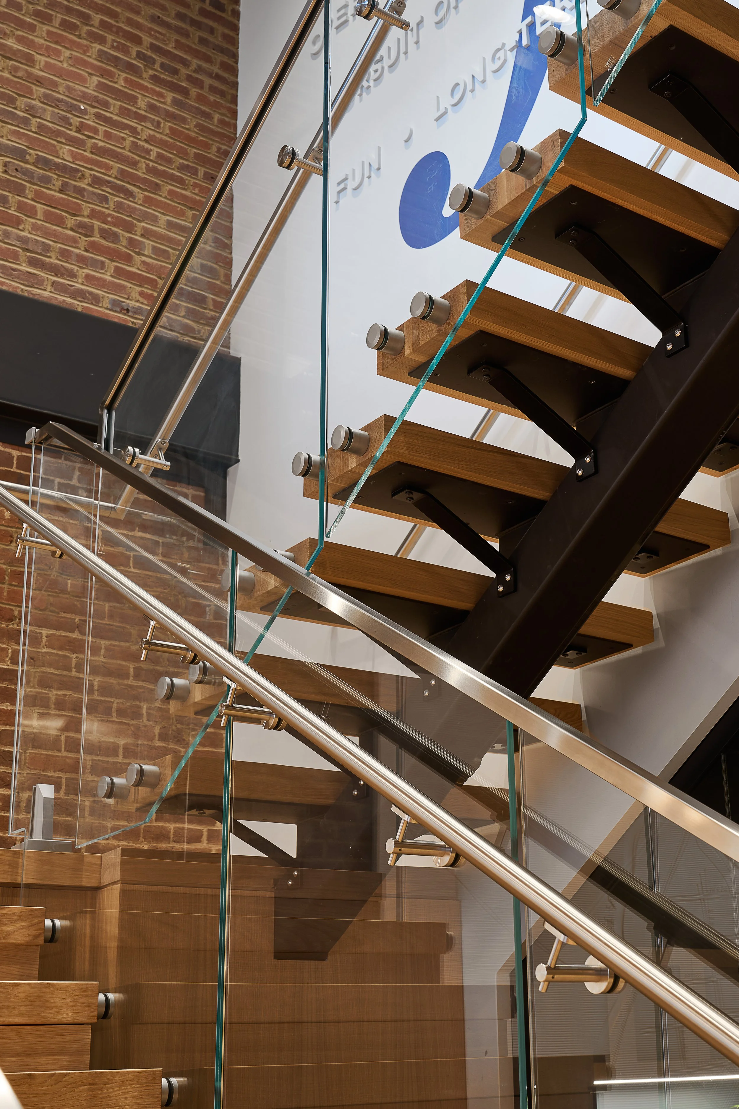 Modern staircase with wooden steps, glass side panels, metal handrails, and brick wall background.