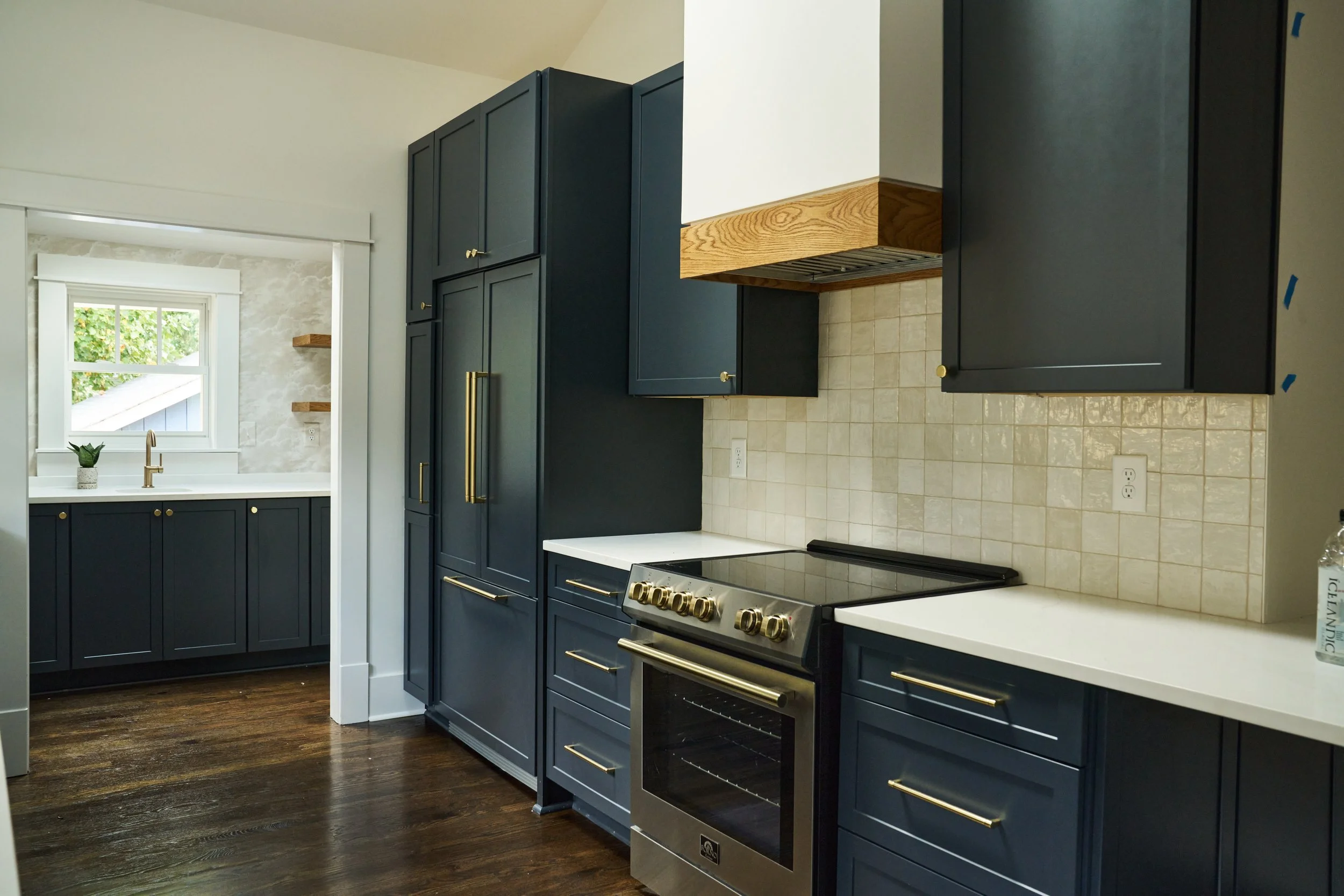 Kitchen with dark blue cabinets, white countertops, beige tiled backsplash, and stainless steel oven and range. There is a window with white trim and a small plant on the windowsill.