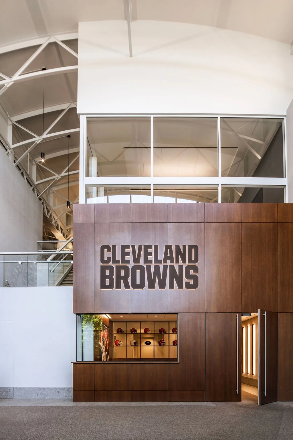 Interior view of the Cleveland Browns facility with a wooden wall displaying the team name and a display case with football helmets.