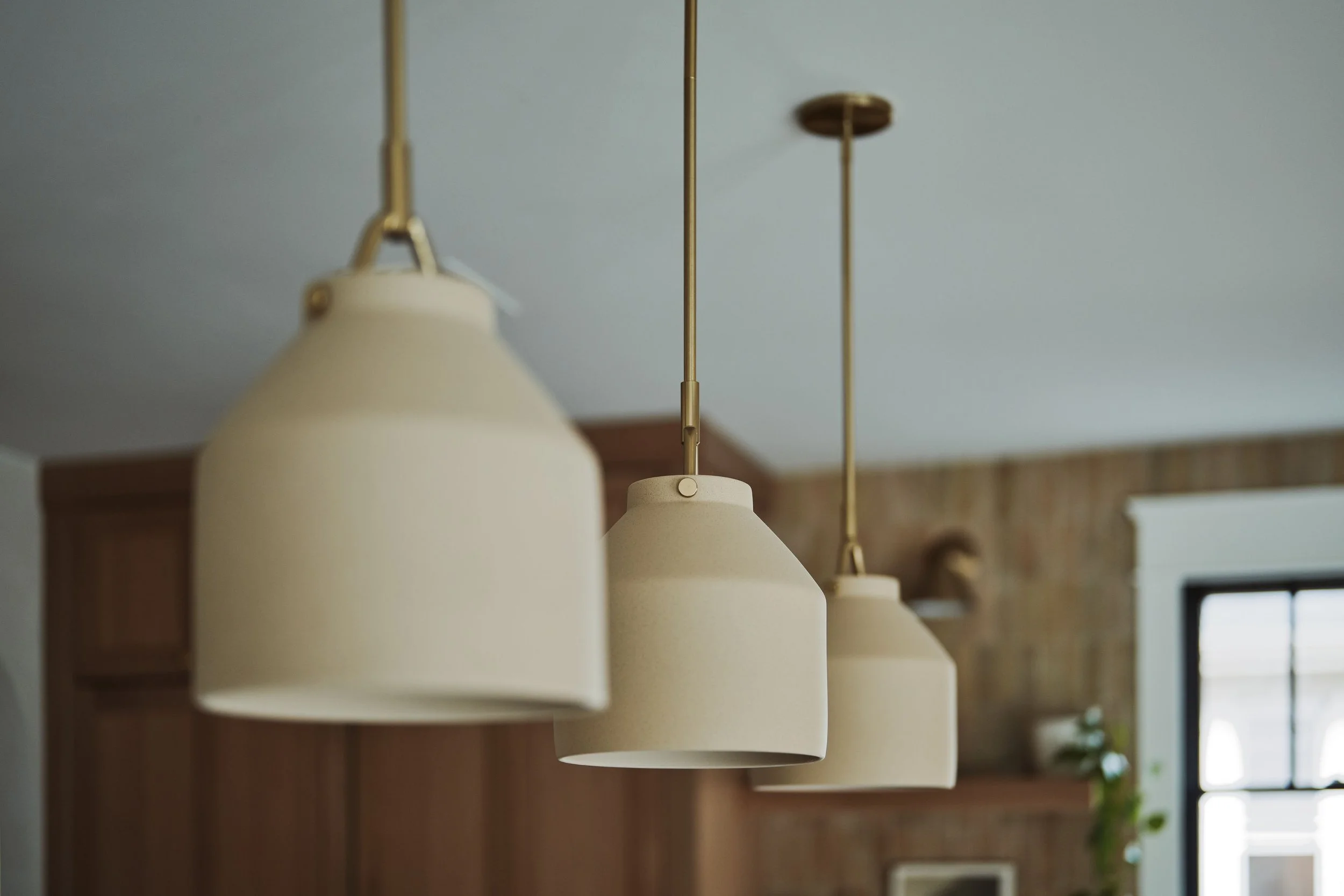 A row of cream-colored pendant lights hanging from a ceiling in a room with wooden and white walls, and windows in the background.