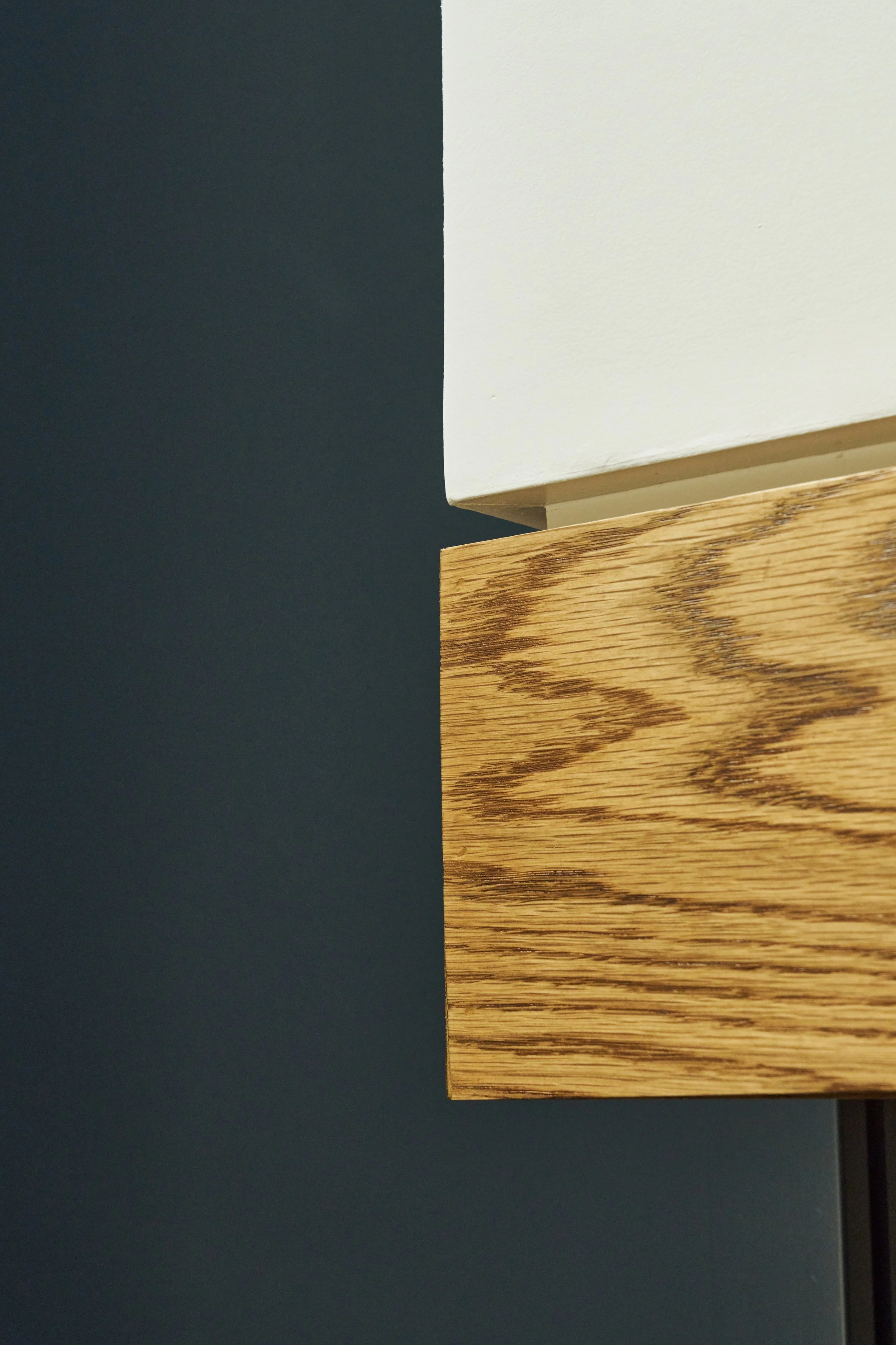 Close-up of a corner of a white painted wall and wooden surface with a dark background.
