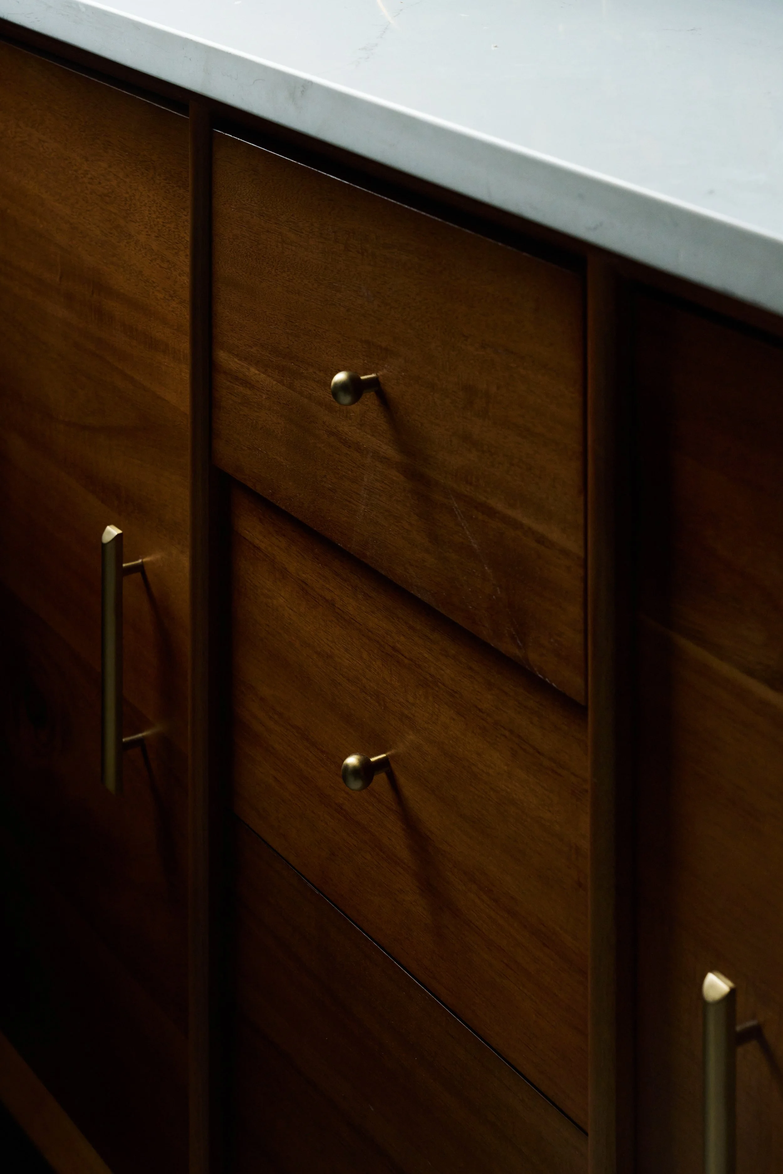 Close-up of a wooden dresser with multiple drawers and metal handles, topped with a light-colored marble or stone surface.