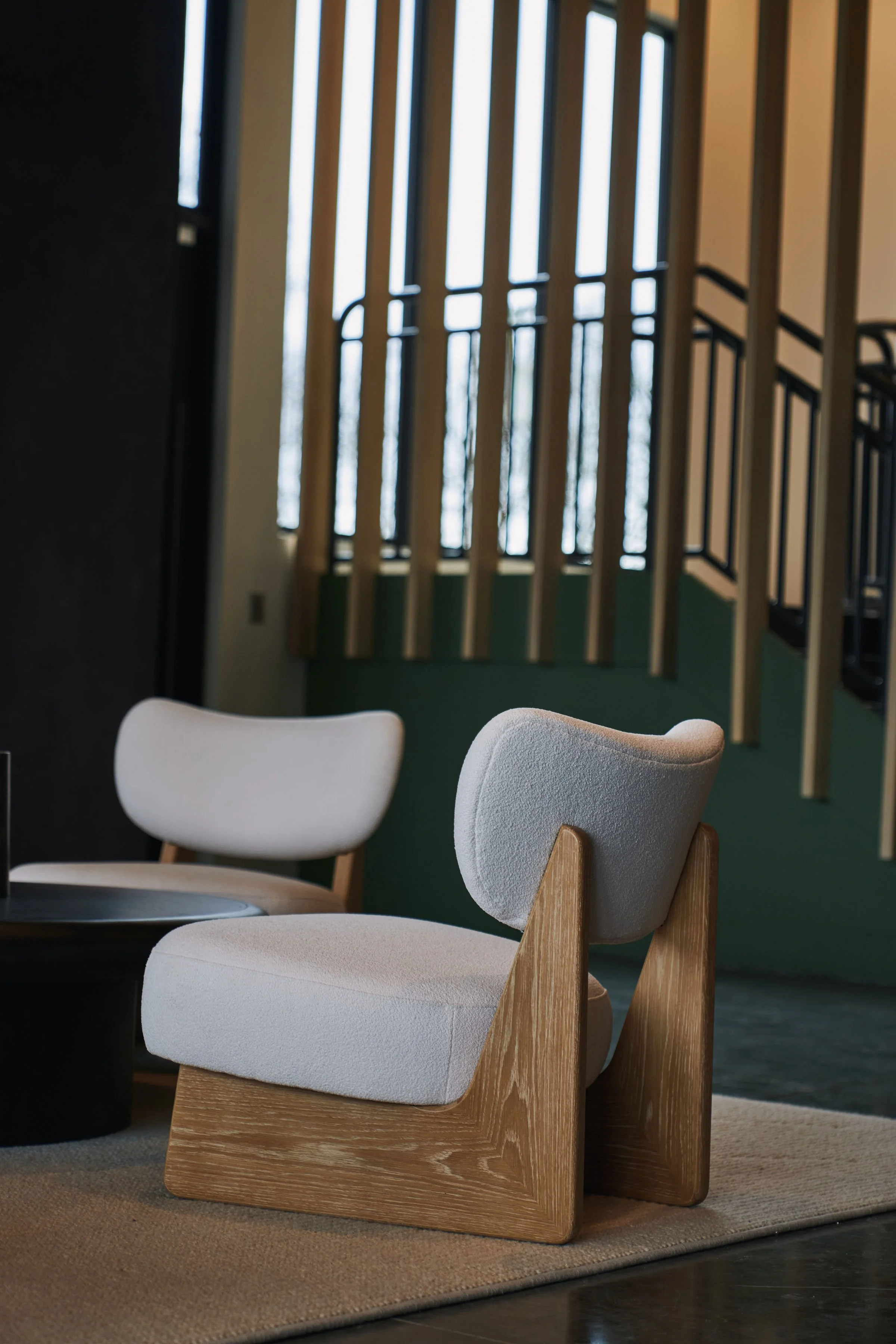 Modern beige armchairs with wooden bases in a cozy room with large windows and a dark side table.