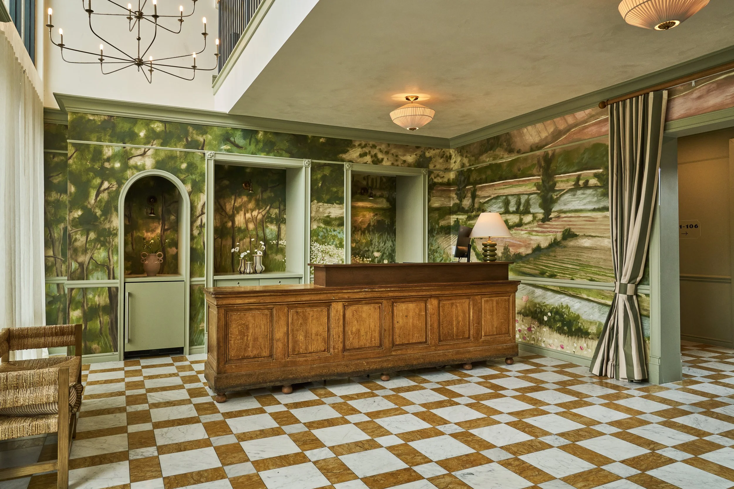 Interior of a building with a reception desk, painting of a landscape on the wall, and tiled checkered floor.