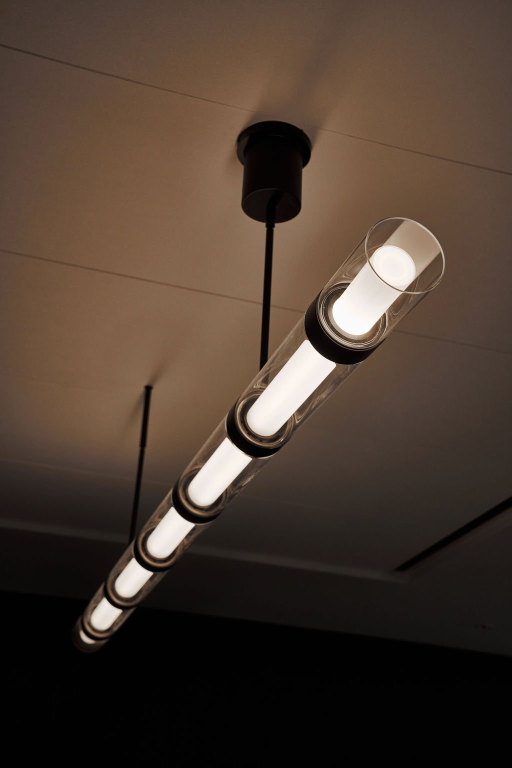 A modern ceiling light fixture with multiple cylindrical LED bulbs encased in clear glass tubes, mounted on a neutral-colored ceiling.