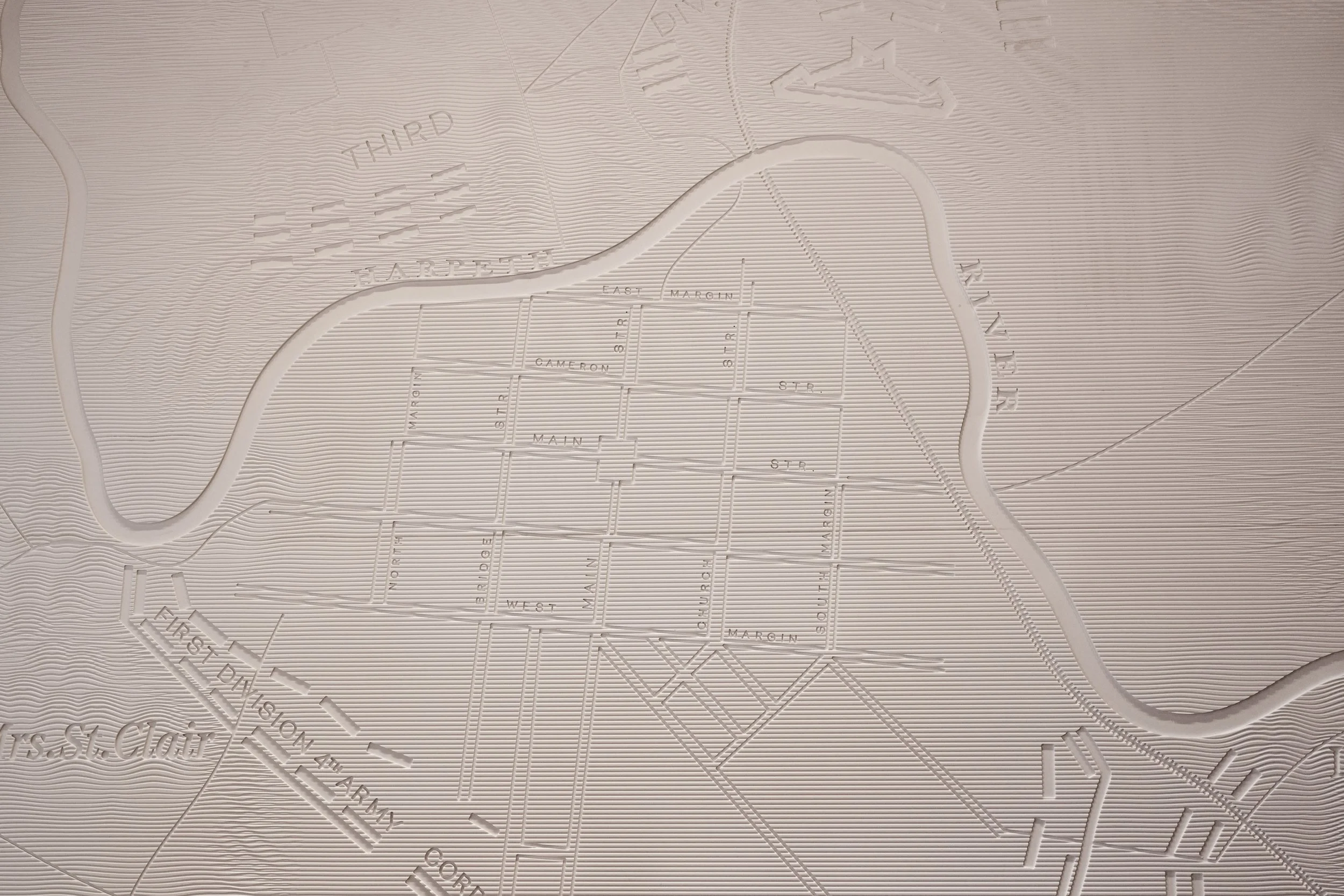 White three-dimensional map of a city showing streets, labeled with names like Main, Cameron, and 8th St. The map includes terrain details, rivers, and surrounding areas.