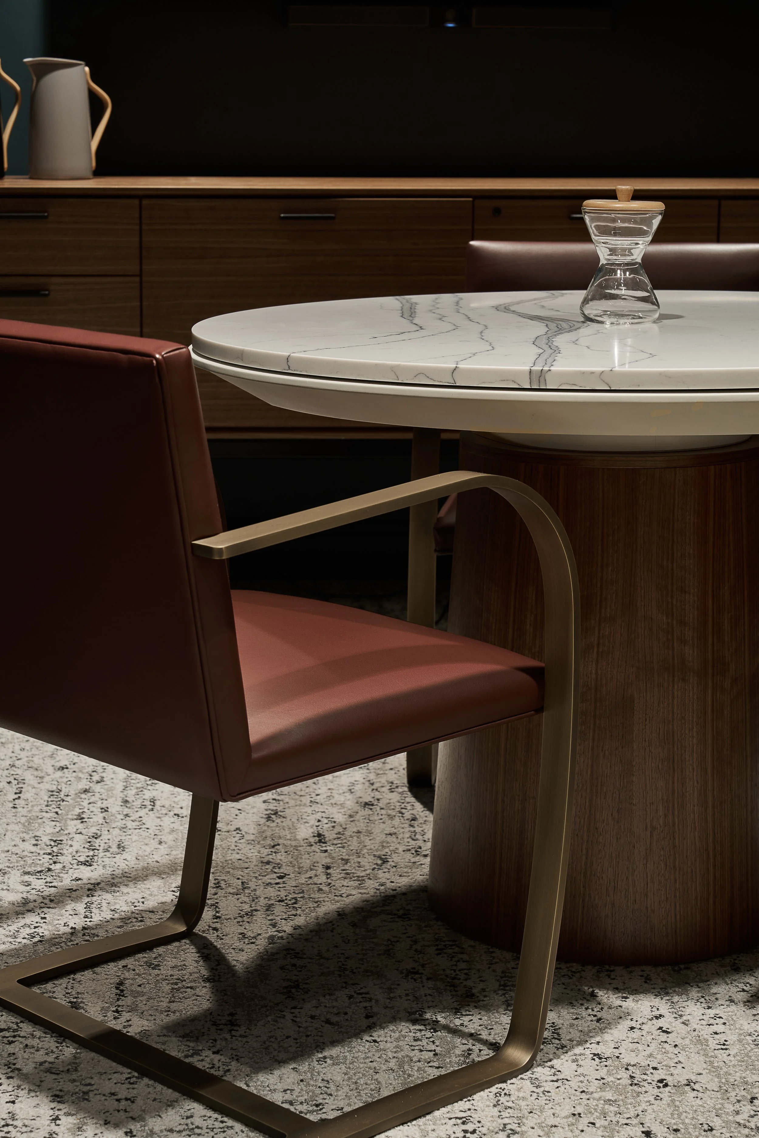 Close-up of a dining table with a marble top, glass sugar bowl with a wooden lid, and a red leather chair with a metal leg in a modern interior space.
