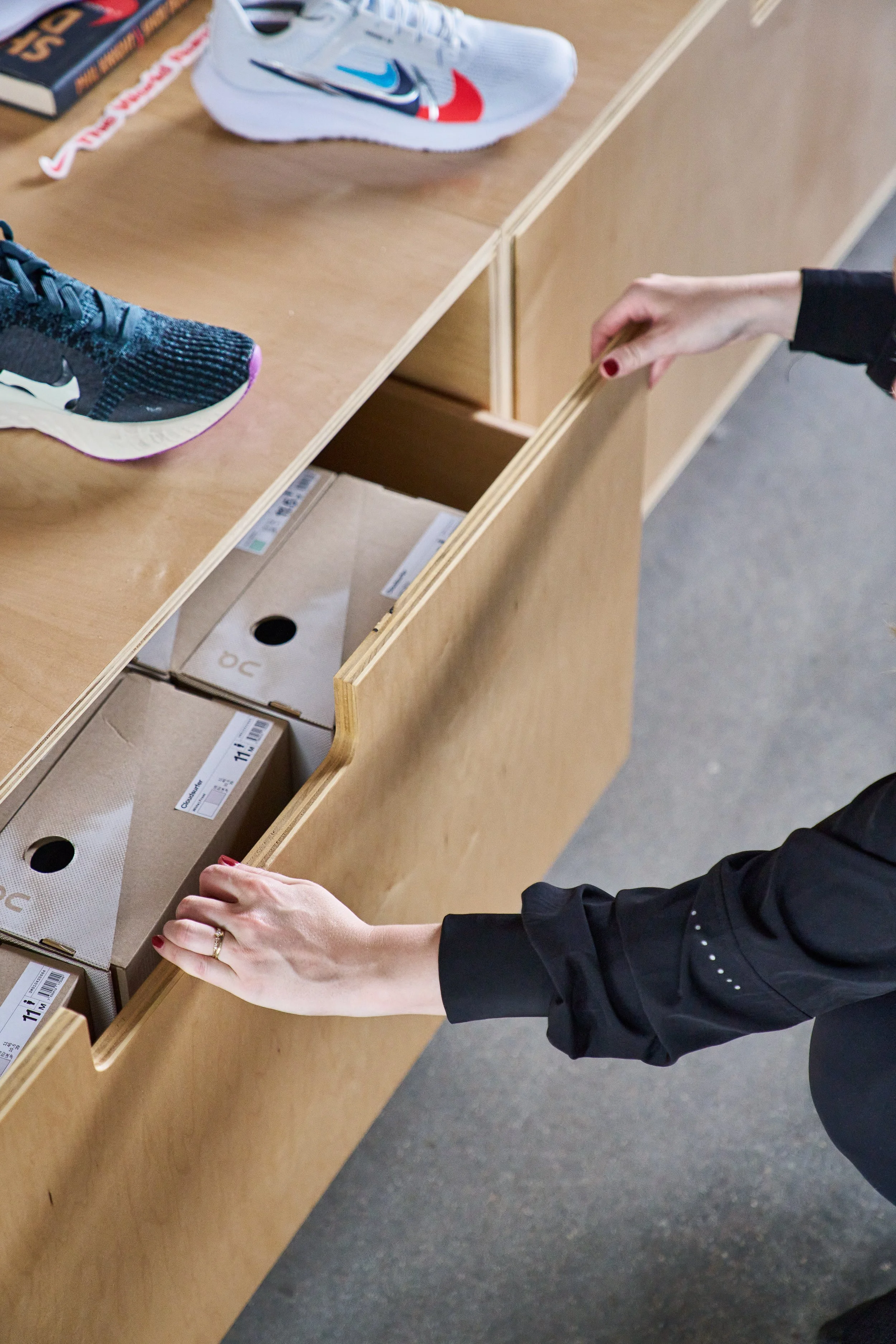 Person opening a wooden drawer in a desk with shoeboxes and shoes on top.
