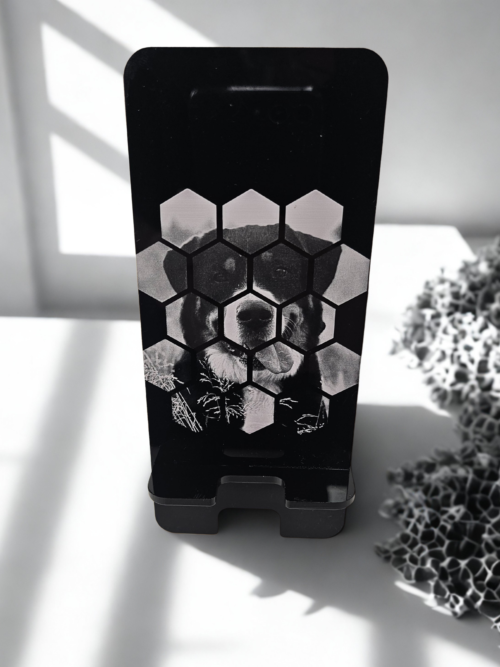A black and white image of a smartphone with a hexagon grid on the screen, displaying a dog's face behind the grid.