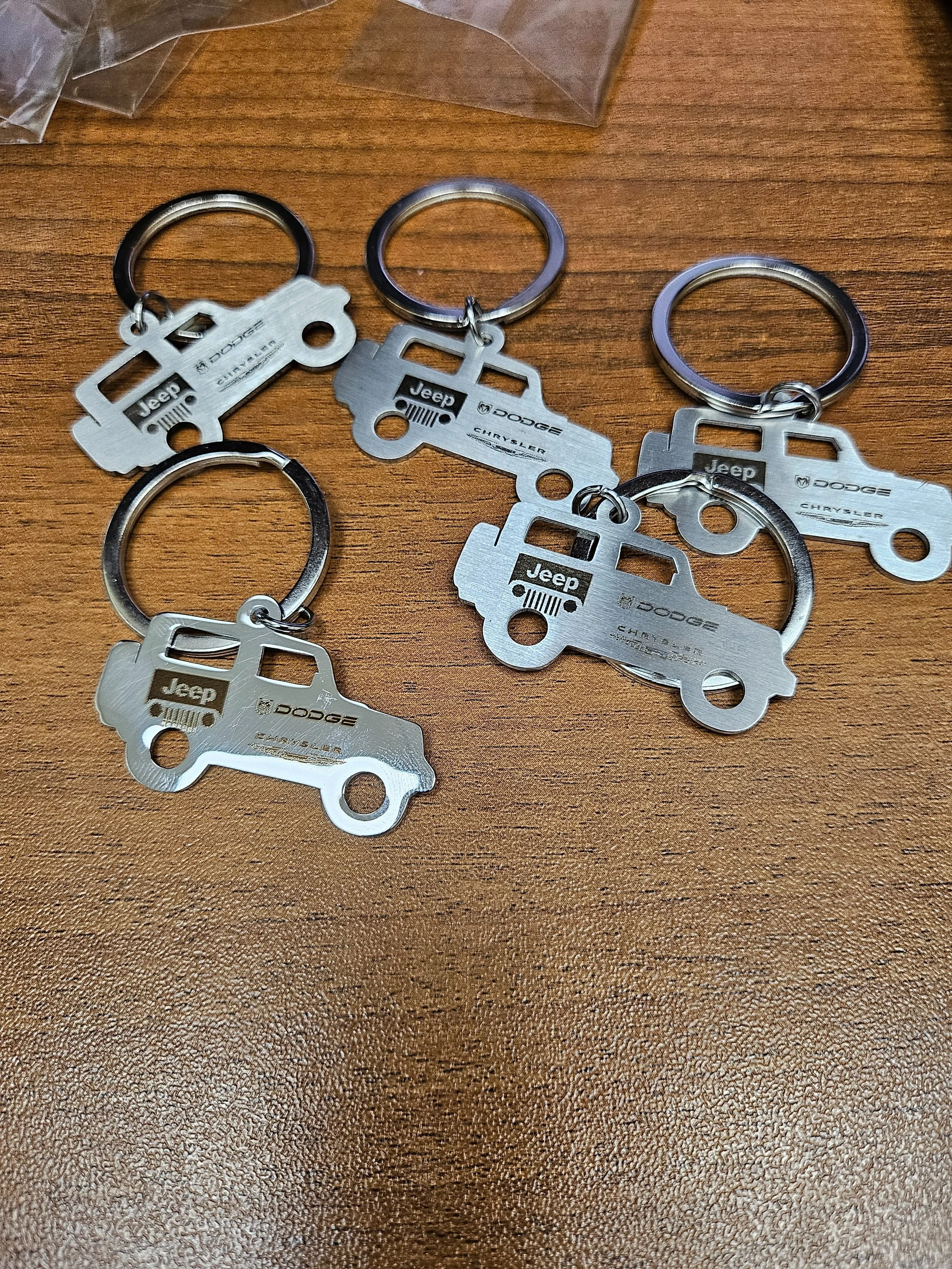 Four metal keychains in the shape of Jeep vehicles on a wooden surface.