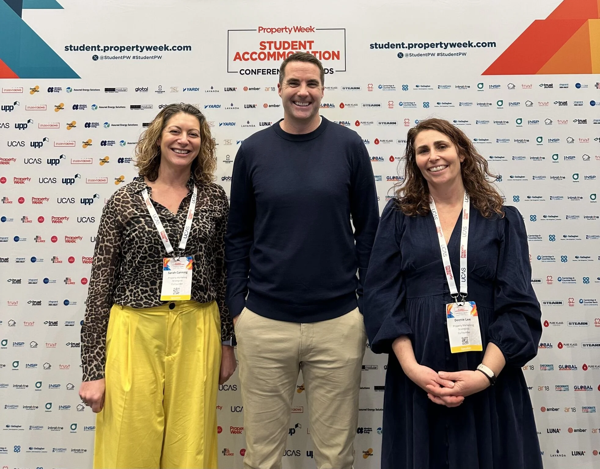 Three people standing in front of a backdrop at an event, smiling, with two women on the left and right and a man in the center. The backdrop features logos and text related to Property Week's Student Accommodation Conference.