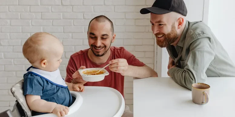 two fathers spoon-feeding their infant